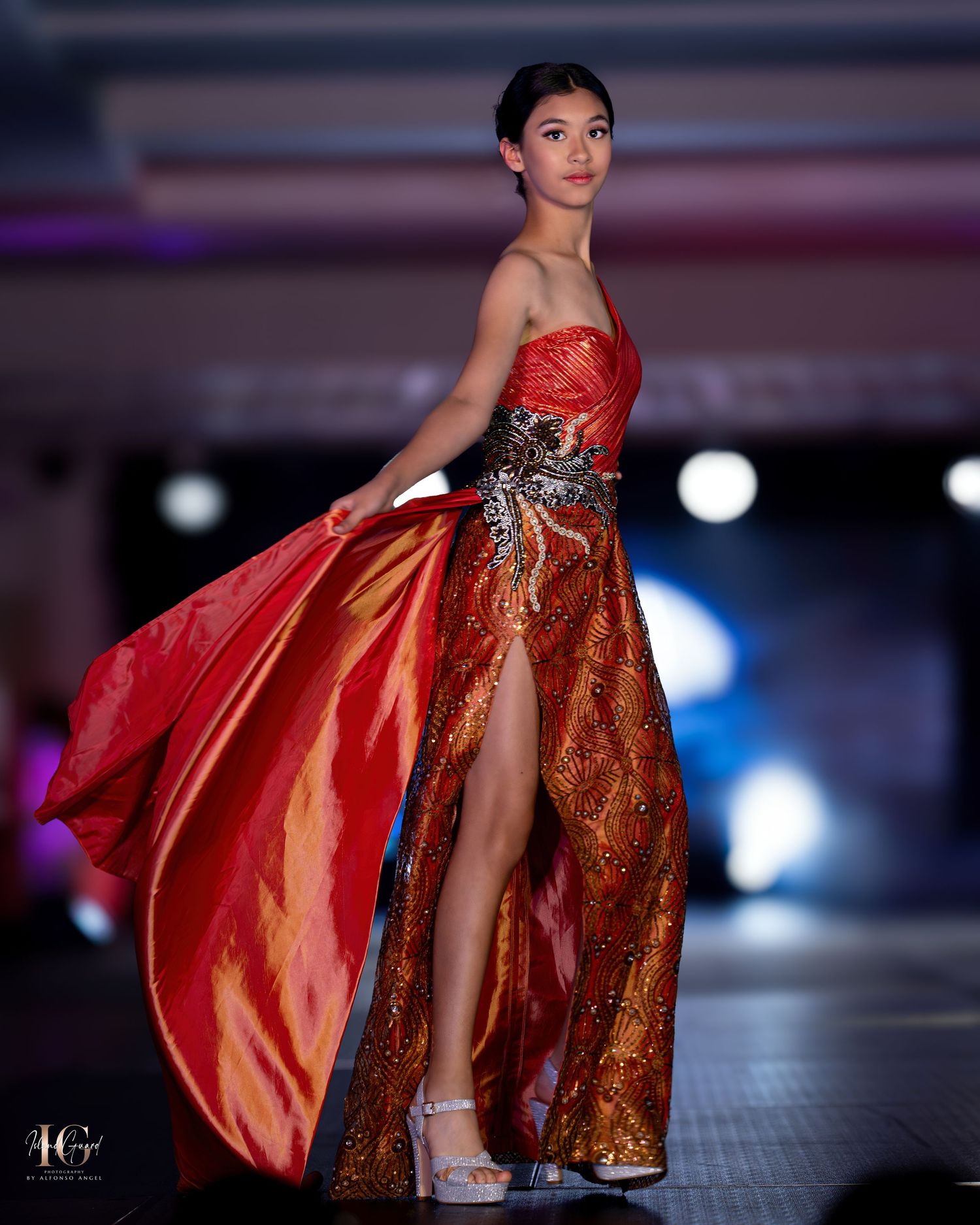 Evening gown with red satin bodice and metallic skirt featuring dramatic side slit on fashion runway.