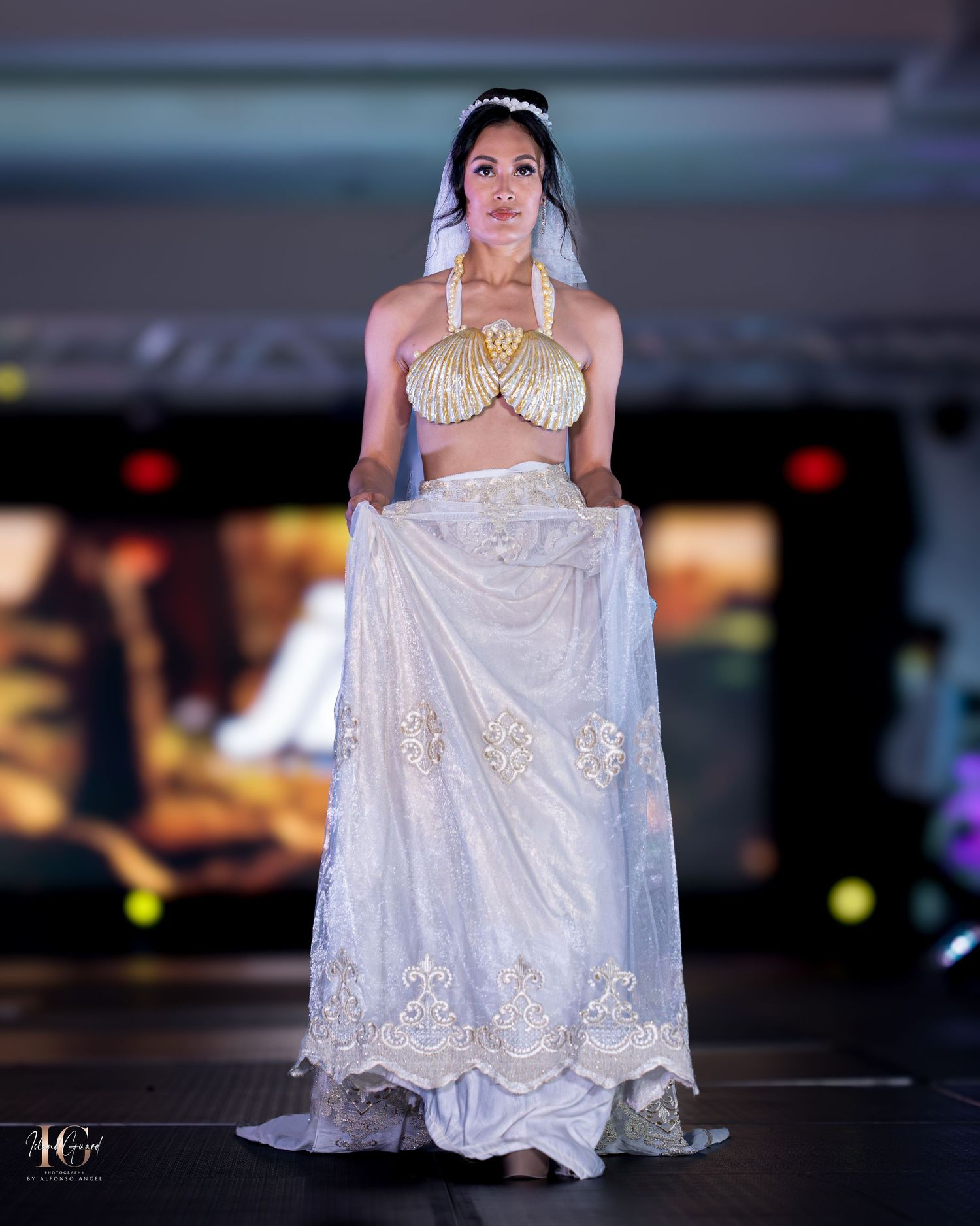 Model presents elegant white lace gown with intricate embroidery details on fashion runway.