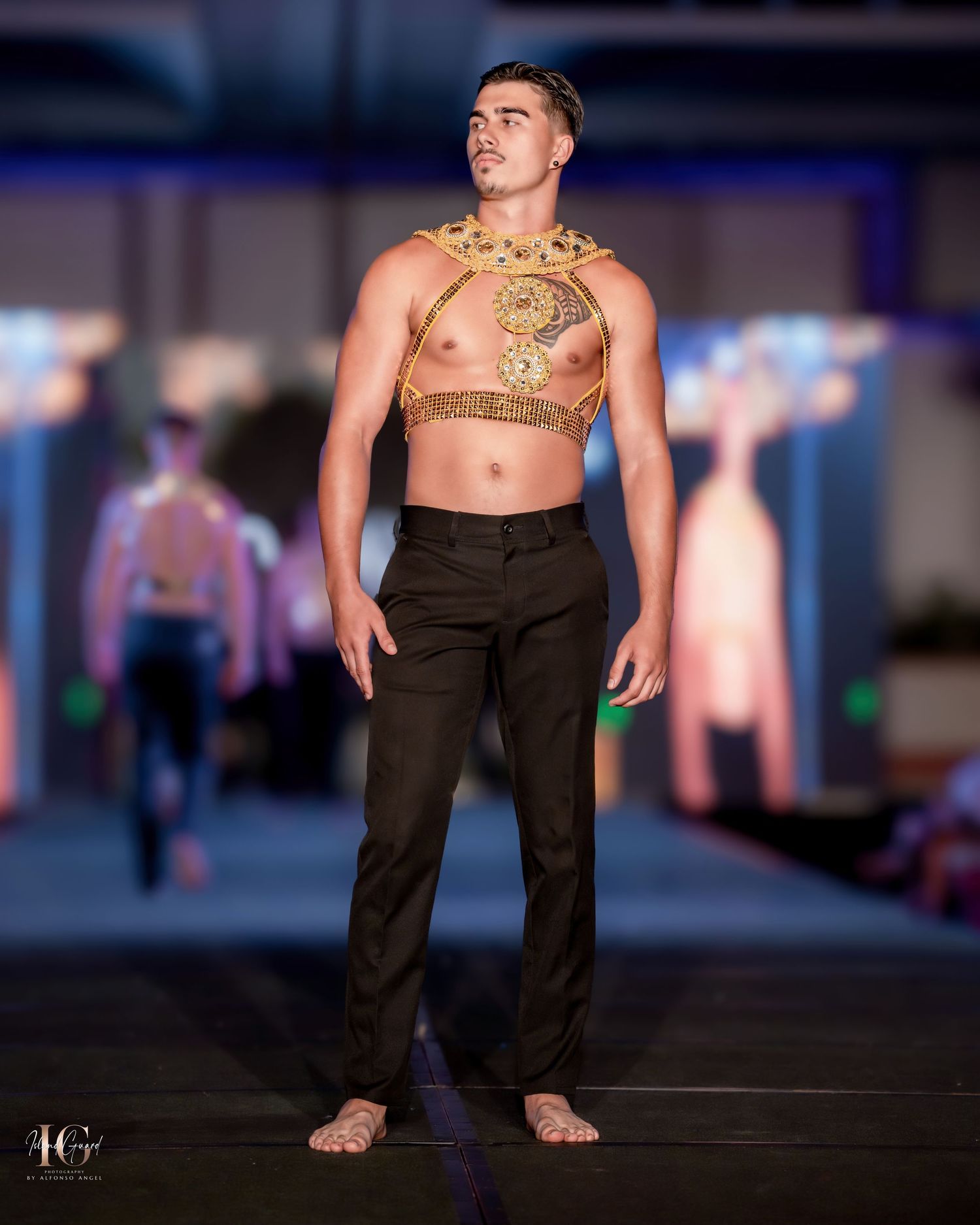Minimalist runway look featuring ornate gold chest piece and dark trousers.