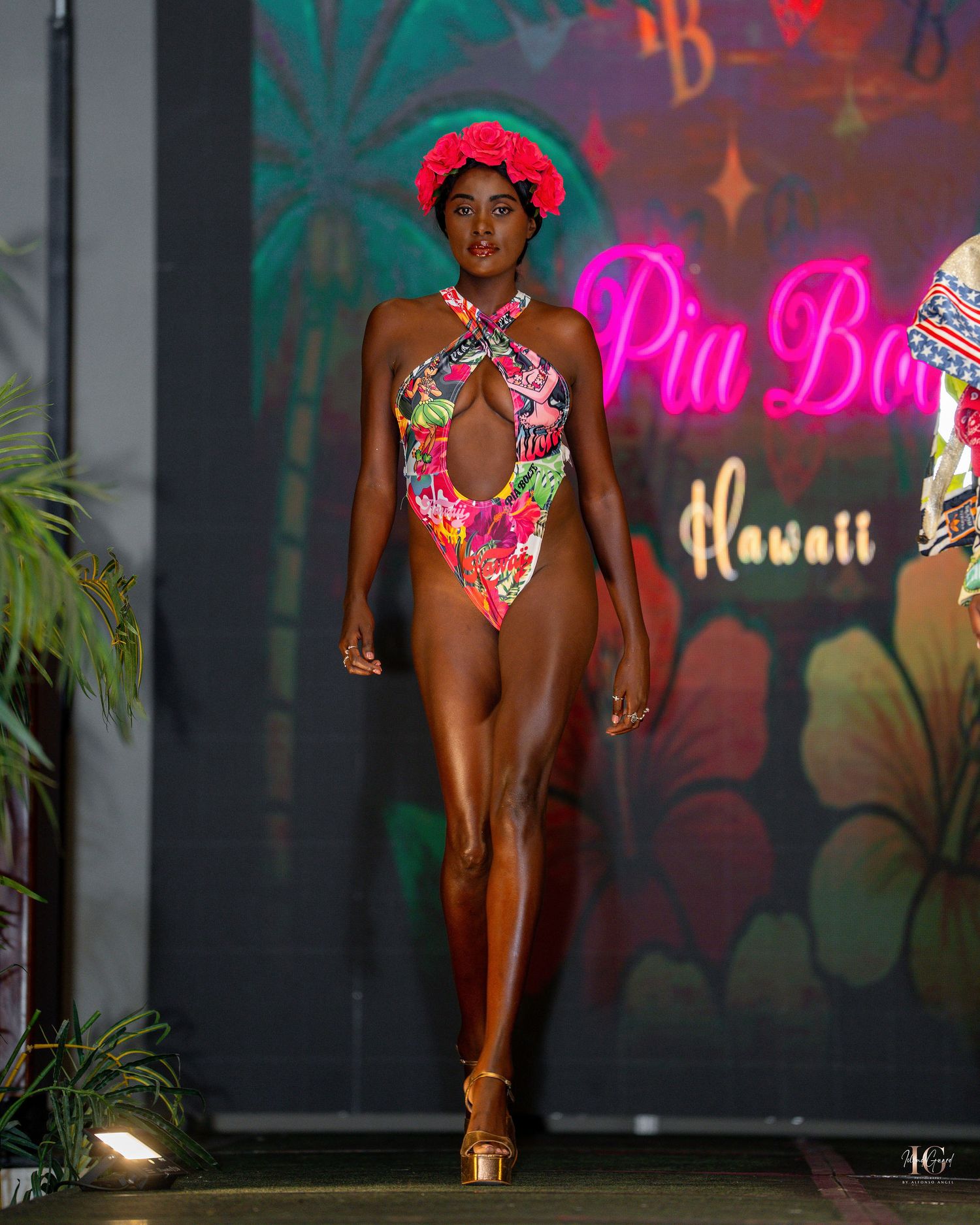 Swimwear fashion show model walks runway in colorful bikini with tropical backdrop and neon lighting.