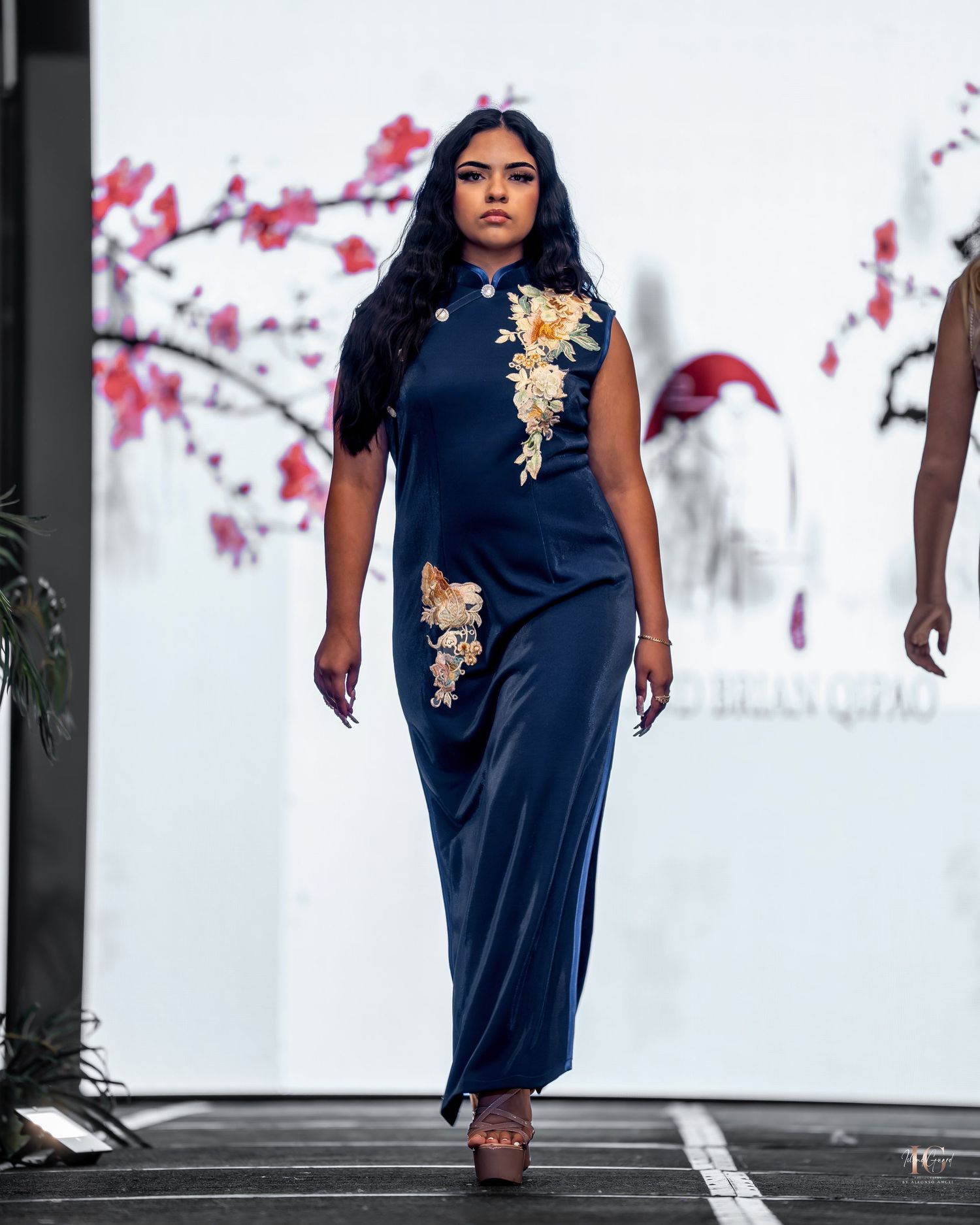 Navy dress with gold floral embellishments styled against a backdrop of pink cherry blossoms in winter.