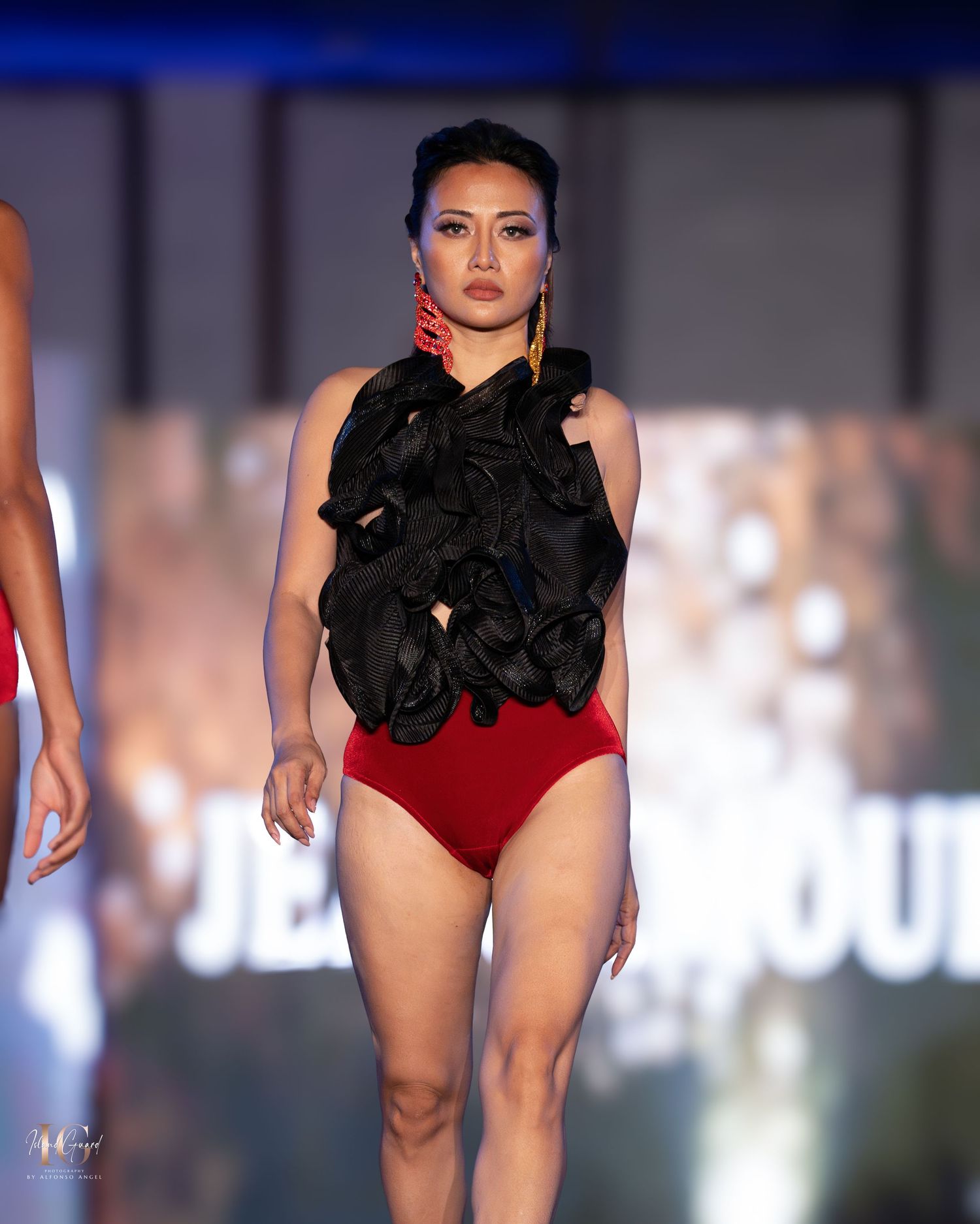 Dramatic red bodysuit with black ruffled neckline detail presented on runway.