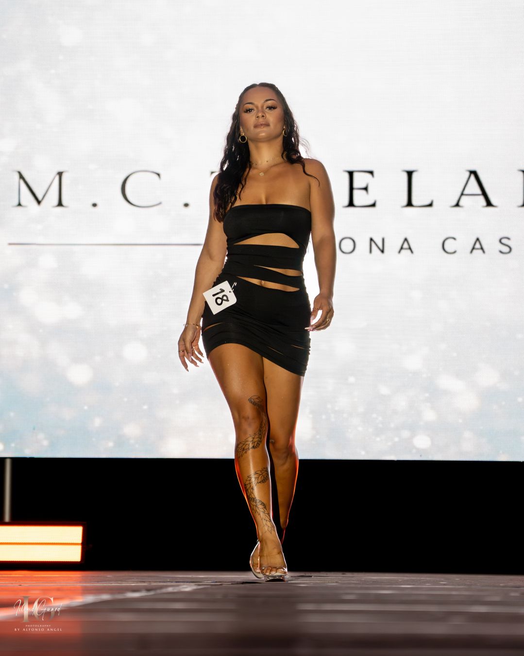 Black cutout mini dress showcased on white runway during fashion show presentation.