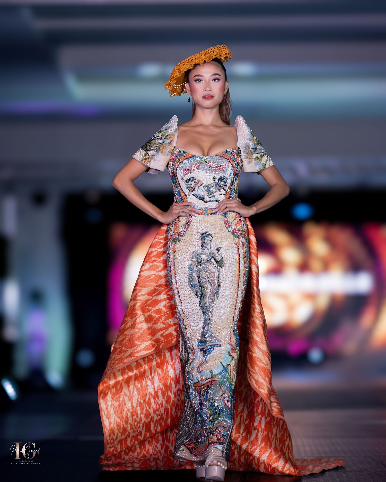 Evening gown with metallic detailing and flowing orange train displayed during luxury fashion event.