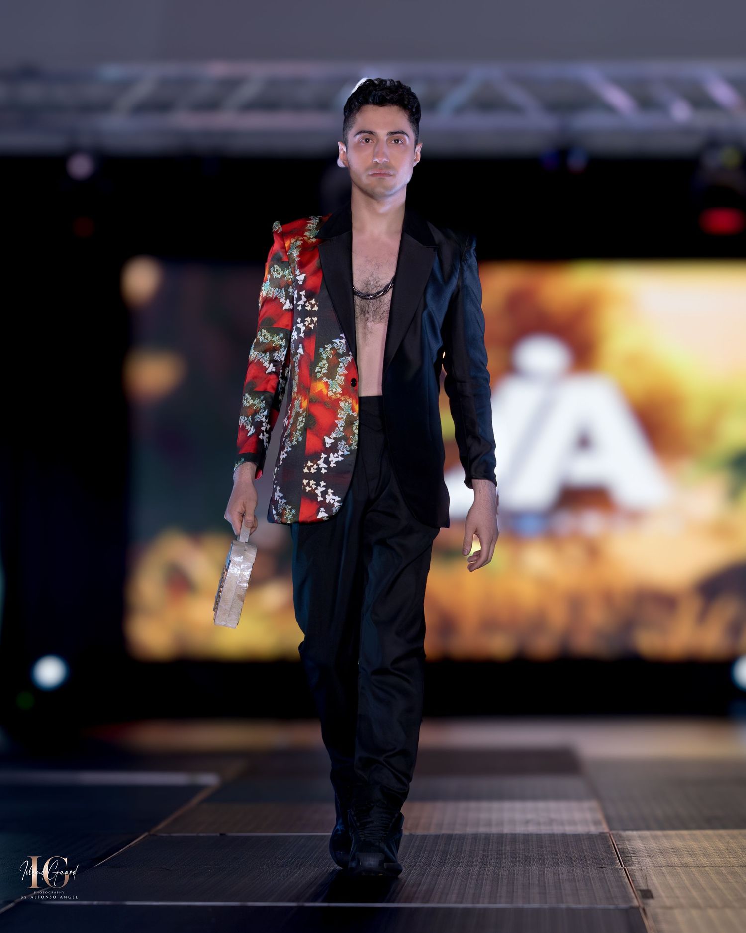 Model wearing black blazer with floral pattern walks confidently down fashion runway.