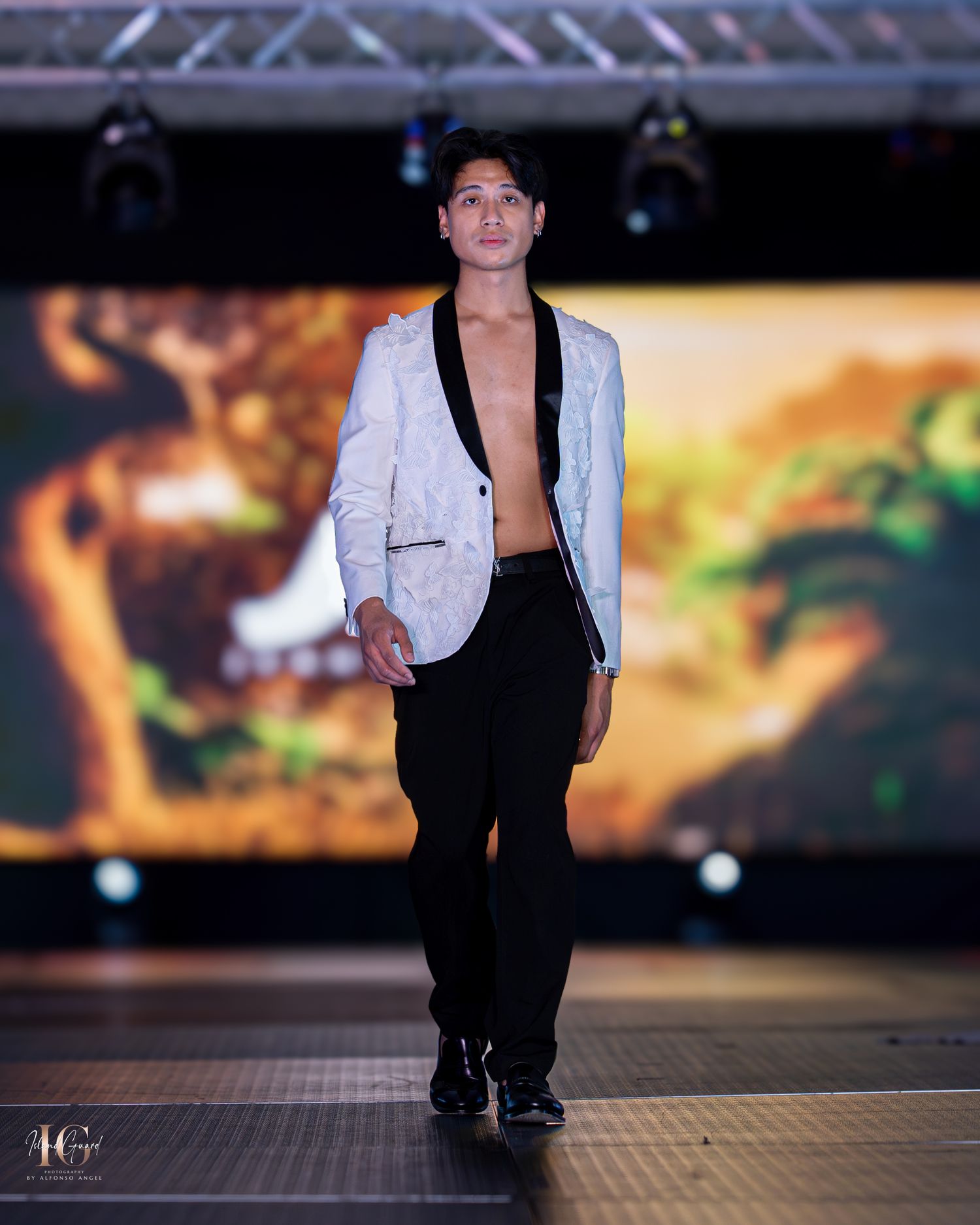 Model wearing black pants and white blazer combination walks fashion runway.