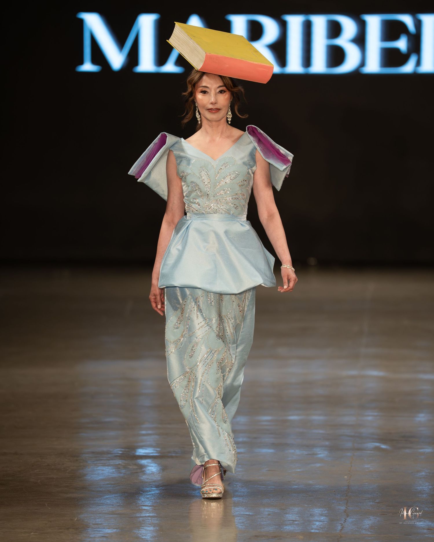 A model walks the runway wearing a flowing light blue evening gown with delicate embellishments during a fashion show.