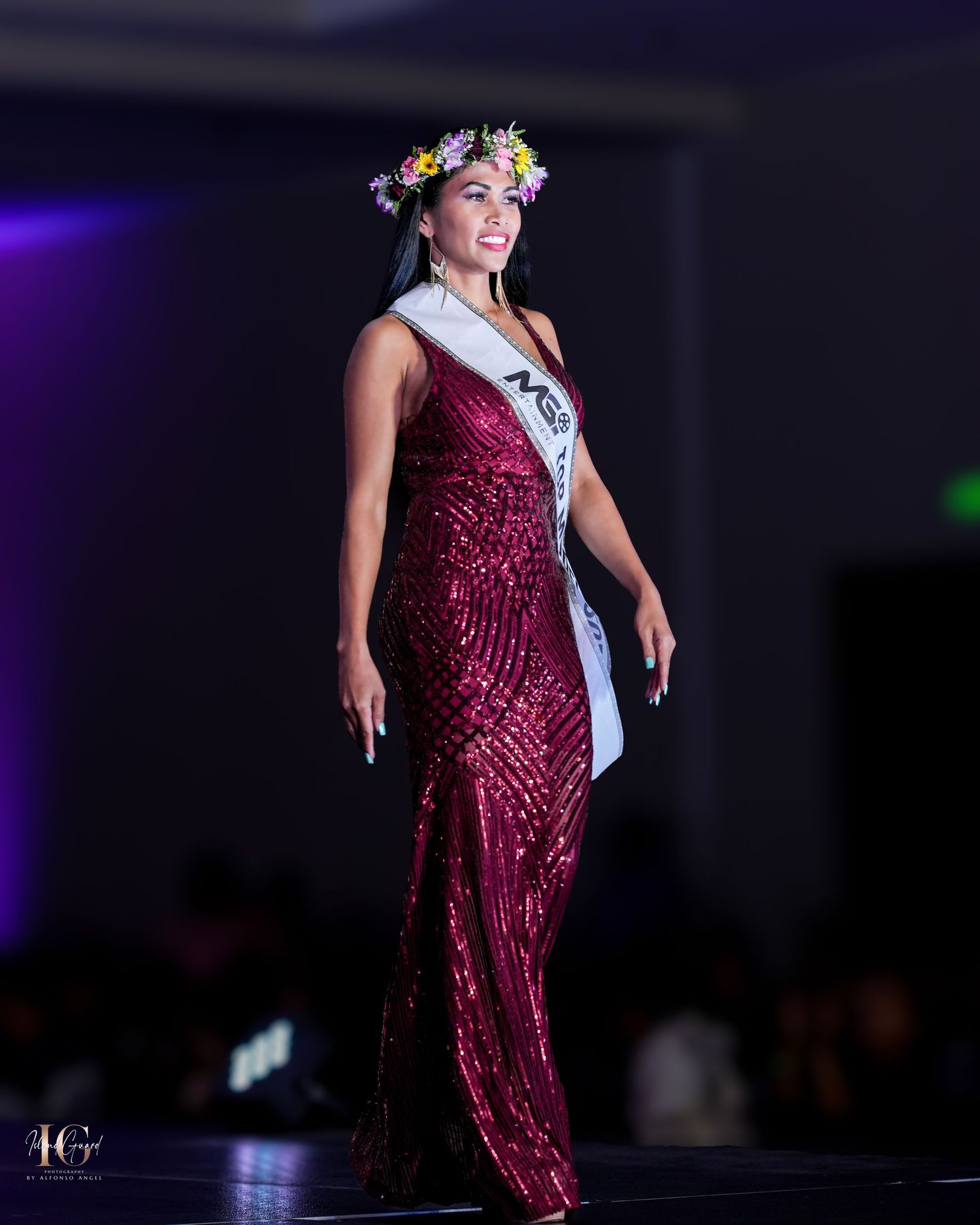 Pageant contestant in burgundy sequin gown and floral crown walks the stage.