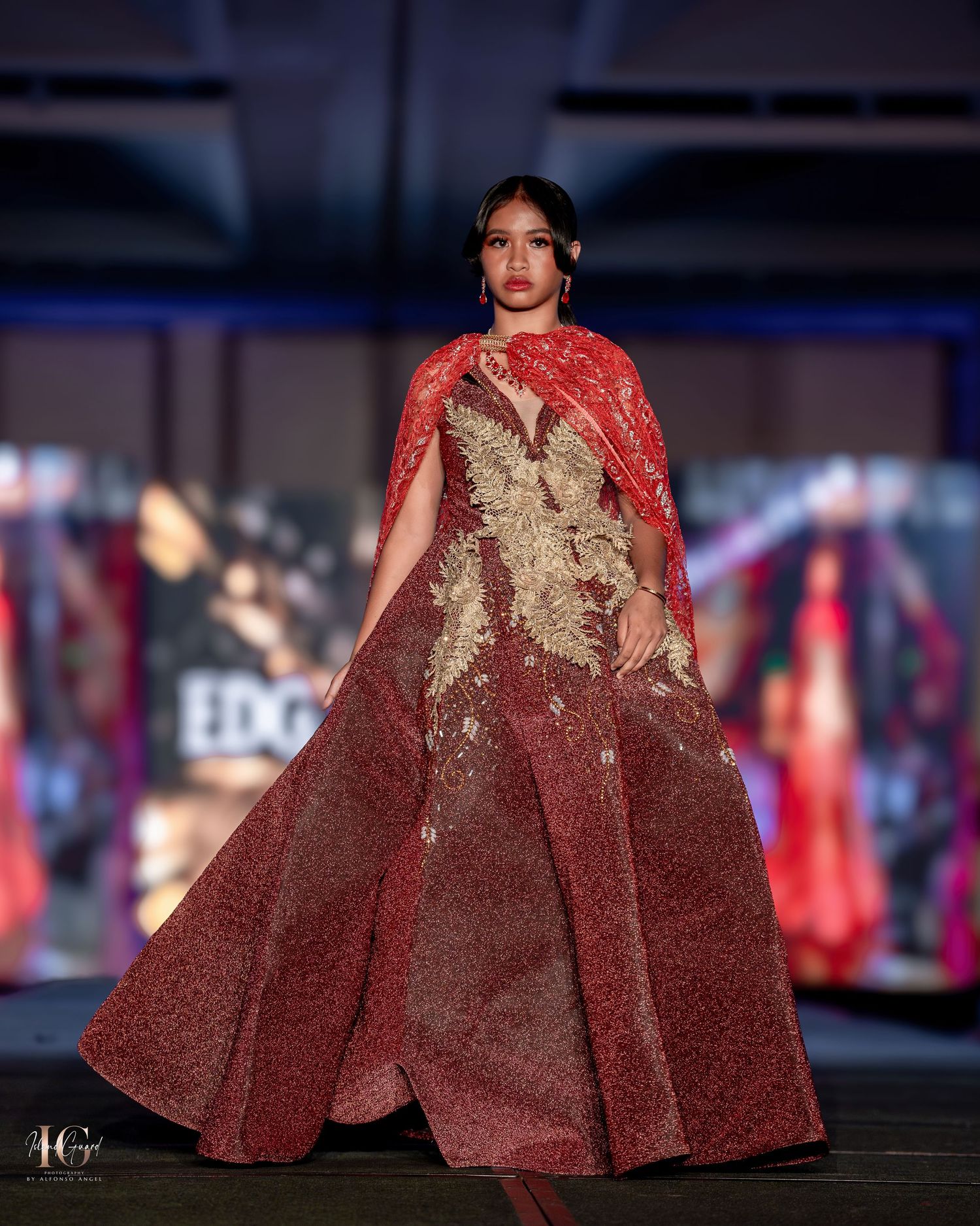 Elegant burgundy evening gown with gold embellishments displayed on fashion runway.