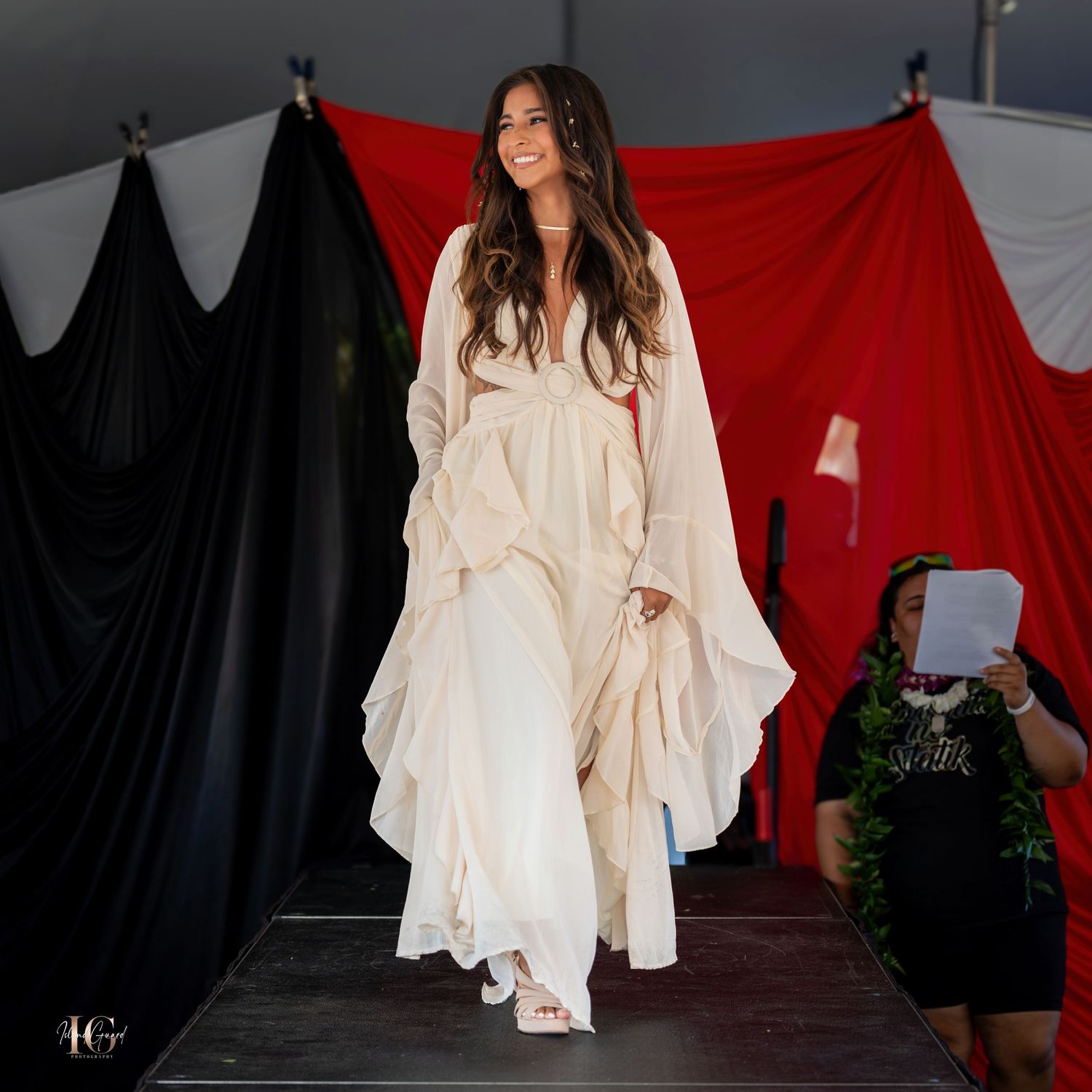 Model in flowing white ensemble poses dramatically against red and black backdrop.