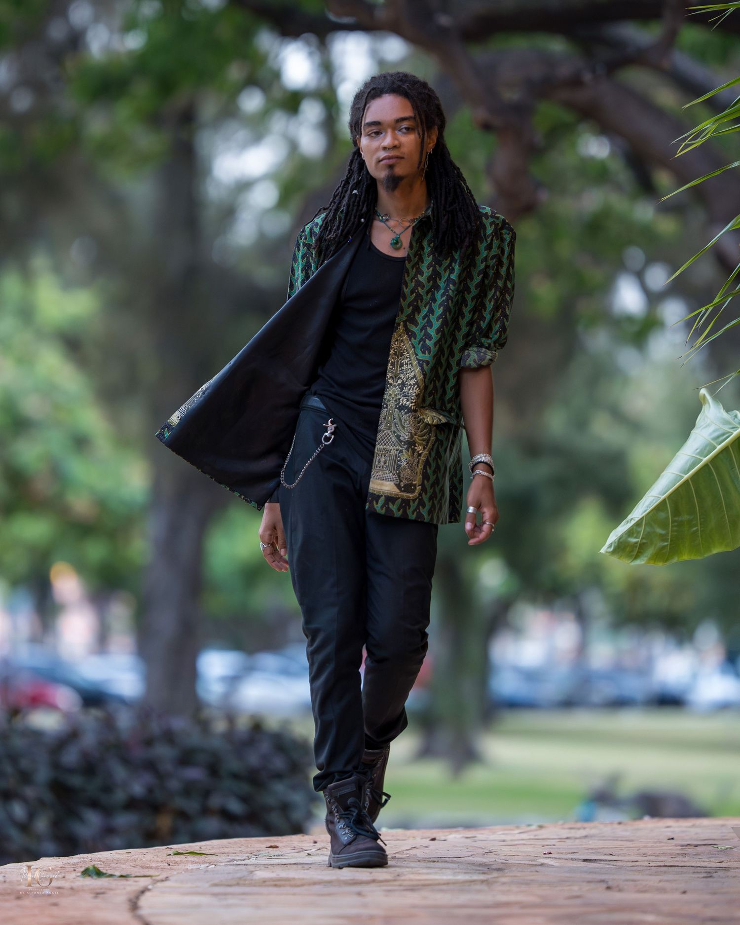 Person in black clothing and long braids walking on a wooden boardwalk in a park setting.