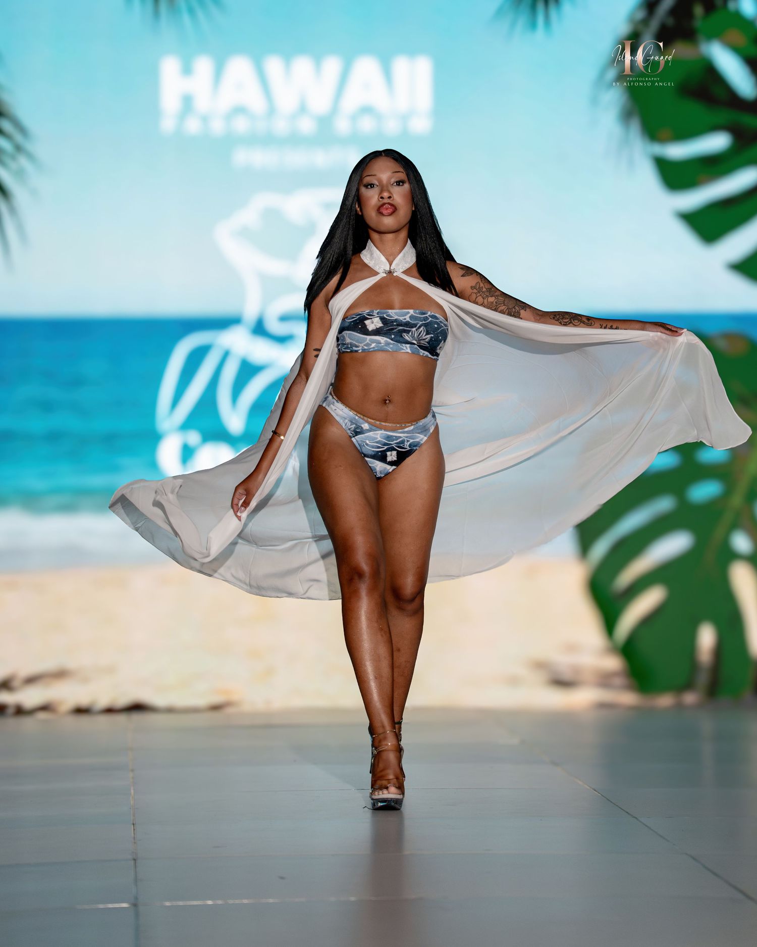 Models showcase swimwear and flowy cover-ups on a tropical runway with beach backdrop at Hawaii Fashion Week.