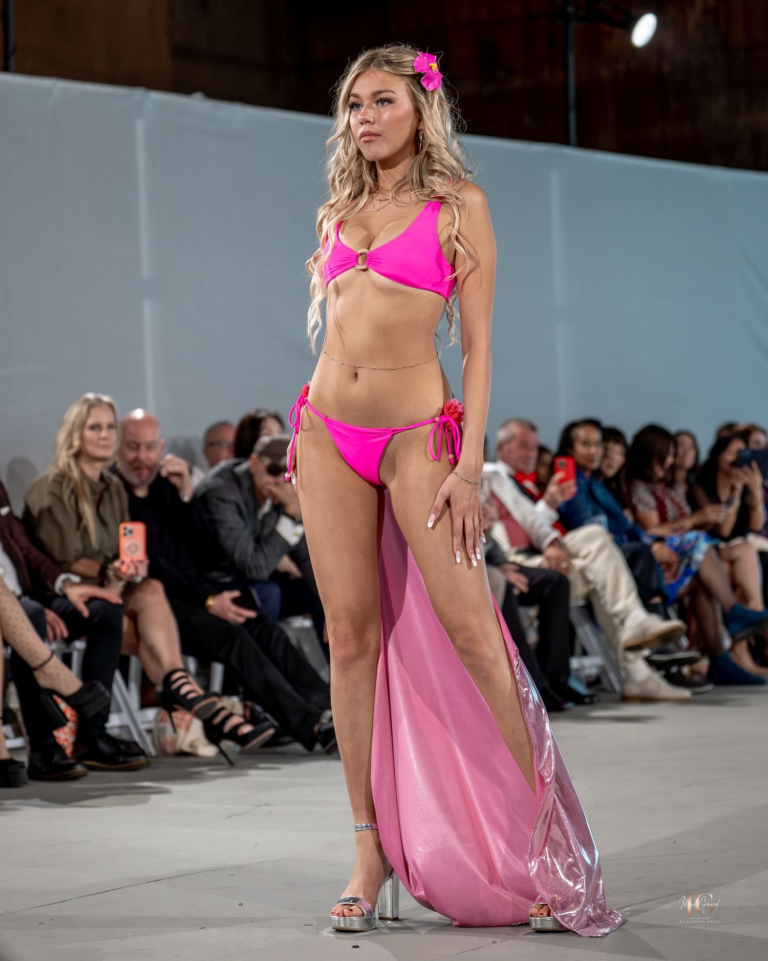 Model walks runway in hot pink swimwear and flowing sheer pink cover-up at fashion show.