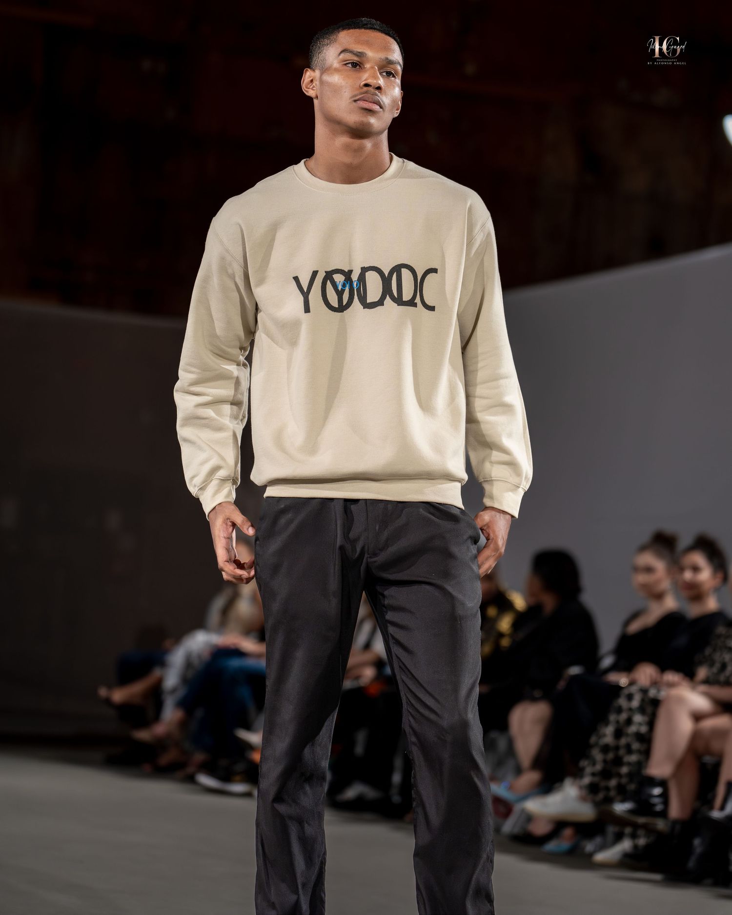 Model walks runway wearing beige YODOC sweatshirt and dark pants during fashion show.