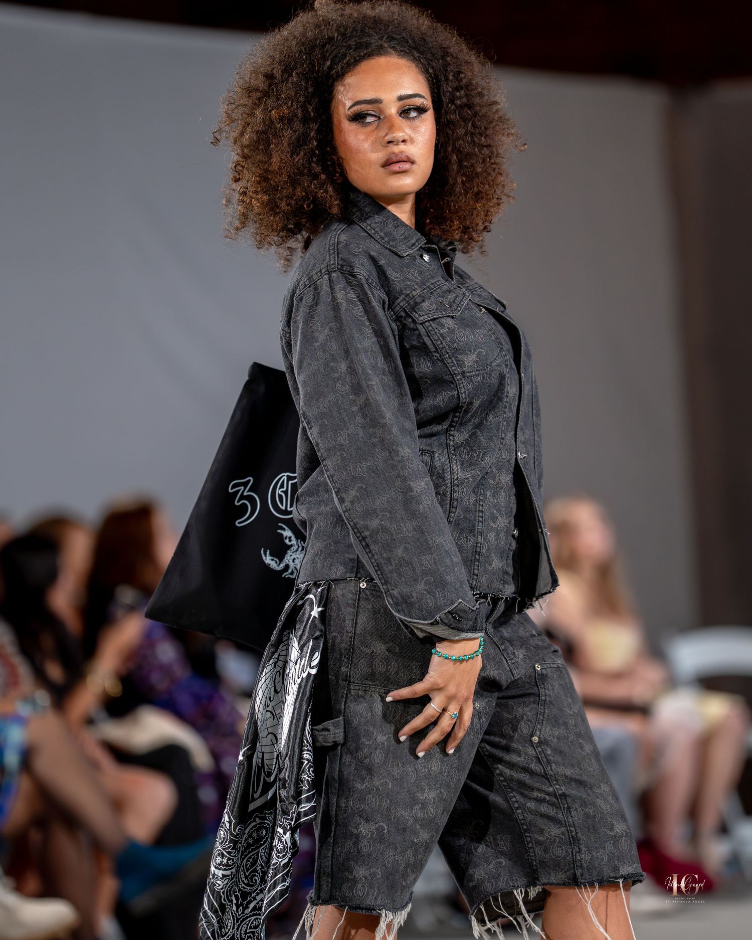 Model walks runway in distressed denim outfit with graffiti print details during fashion show presentation.