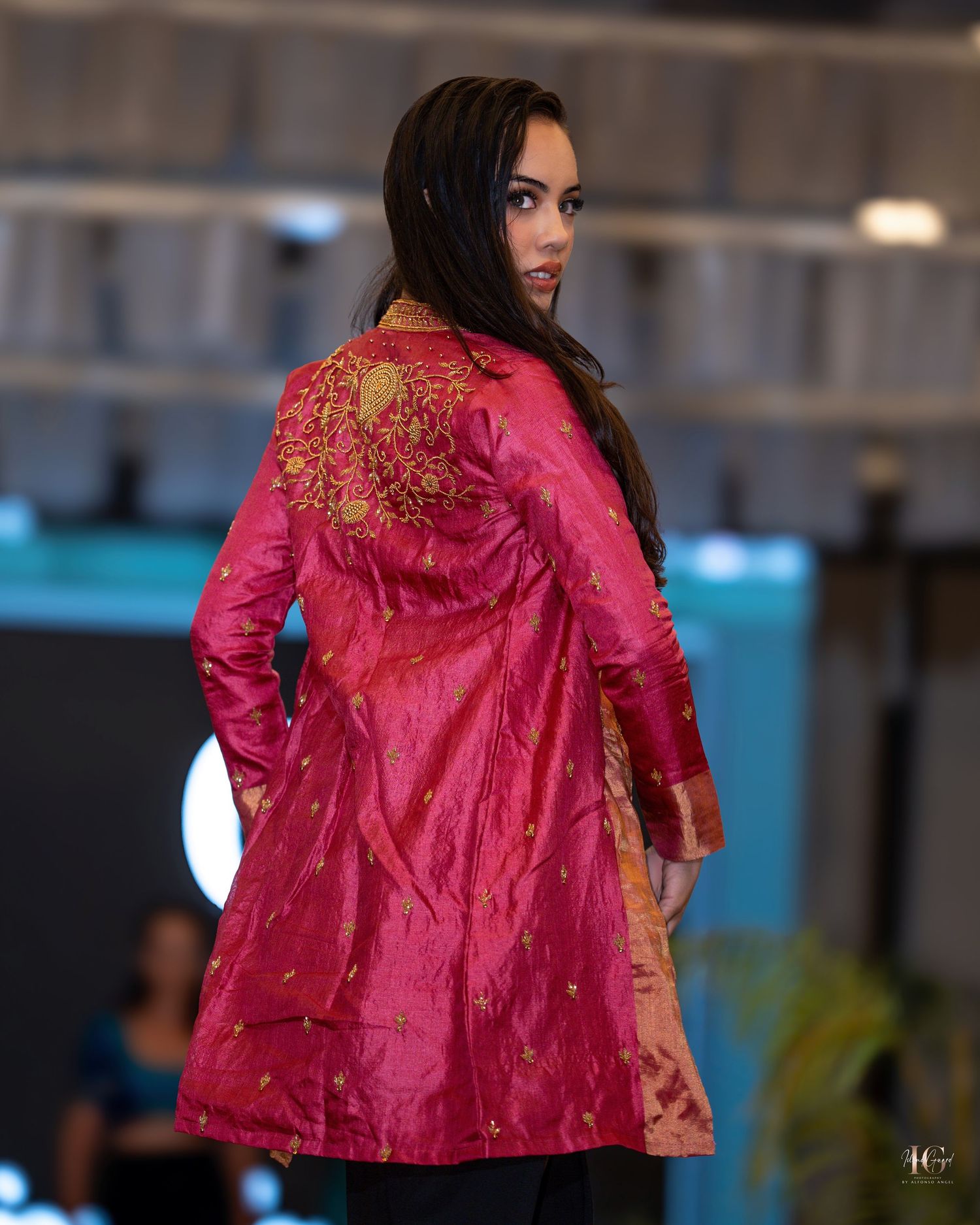 A model walks down the runway wearing a vibrant pink silk jacket with embellished details at a fashion show.