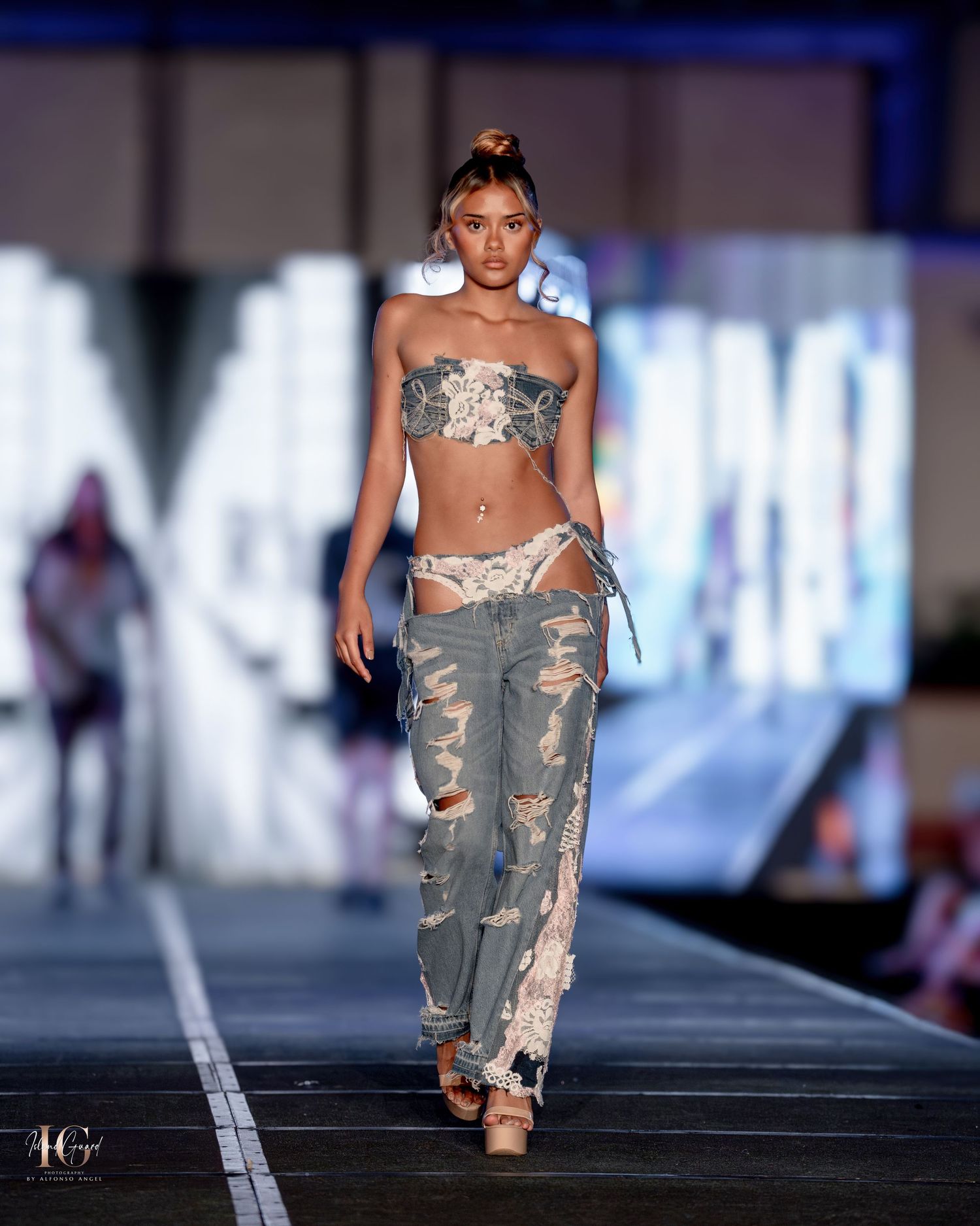 Model presents distressed denim and metallic crop top ensemble on illuminated runway.