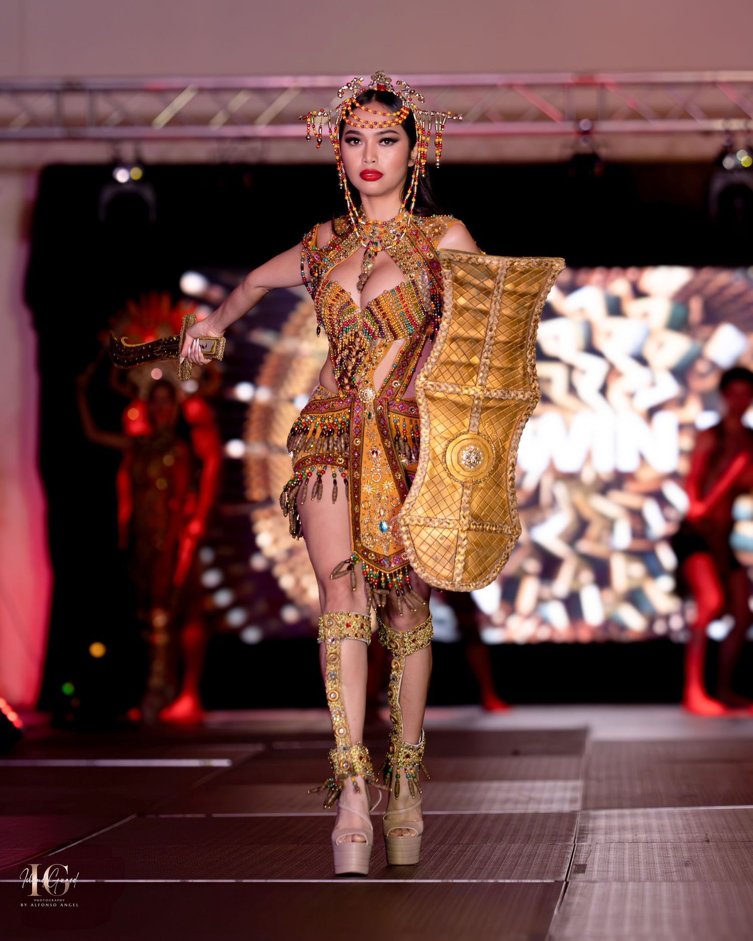Model carrying decorative gold vessel while wearing matching metallic warrior-inspired costume.