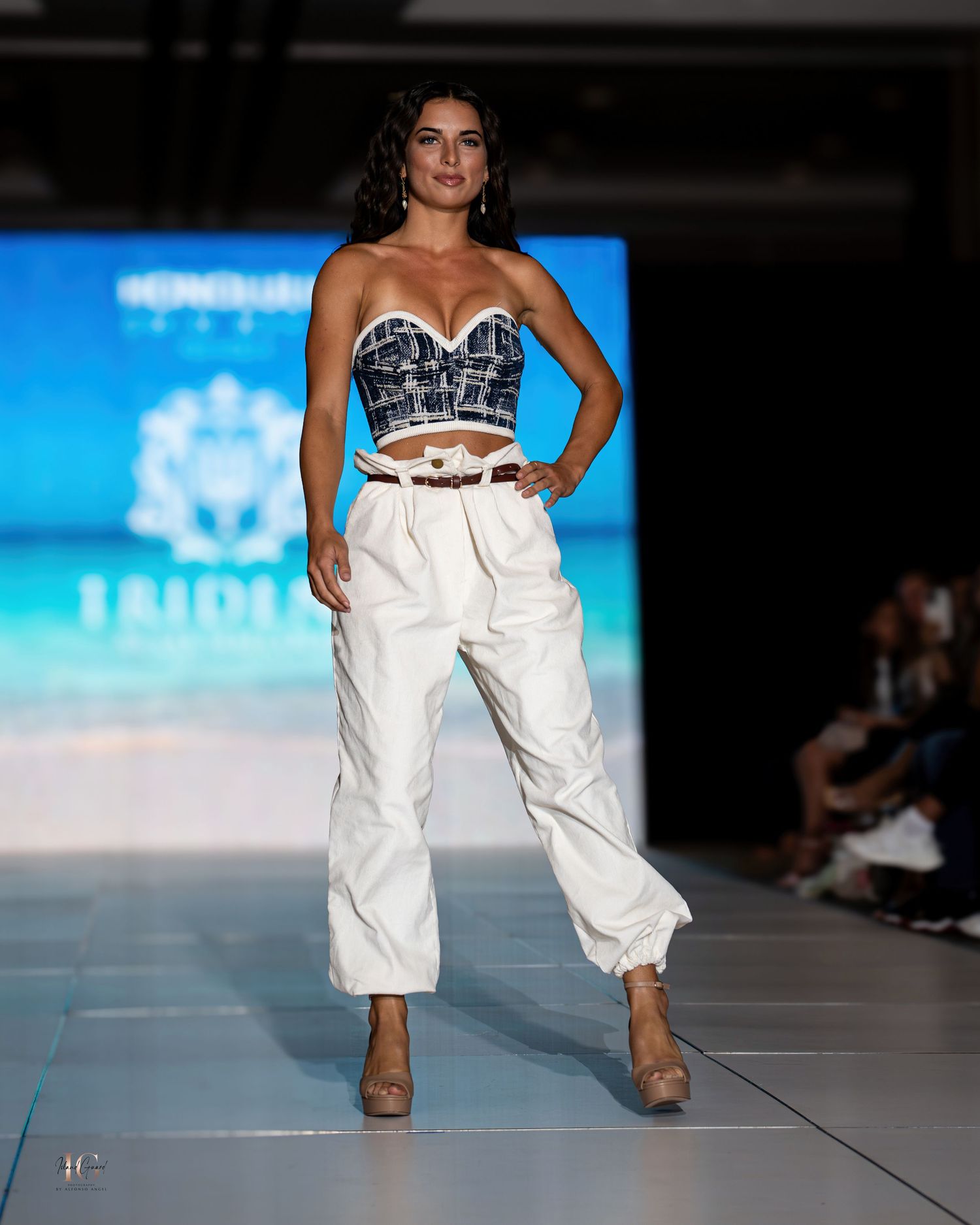 White cargo pants paired with structured corset top shown on fashion runway with beach backdrop.