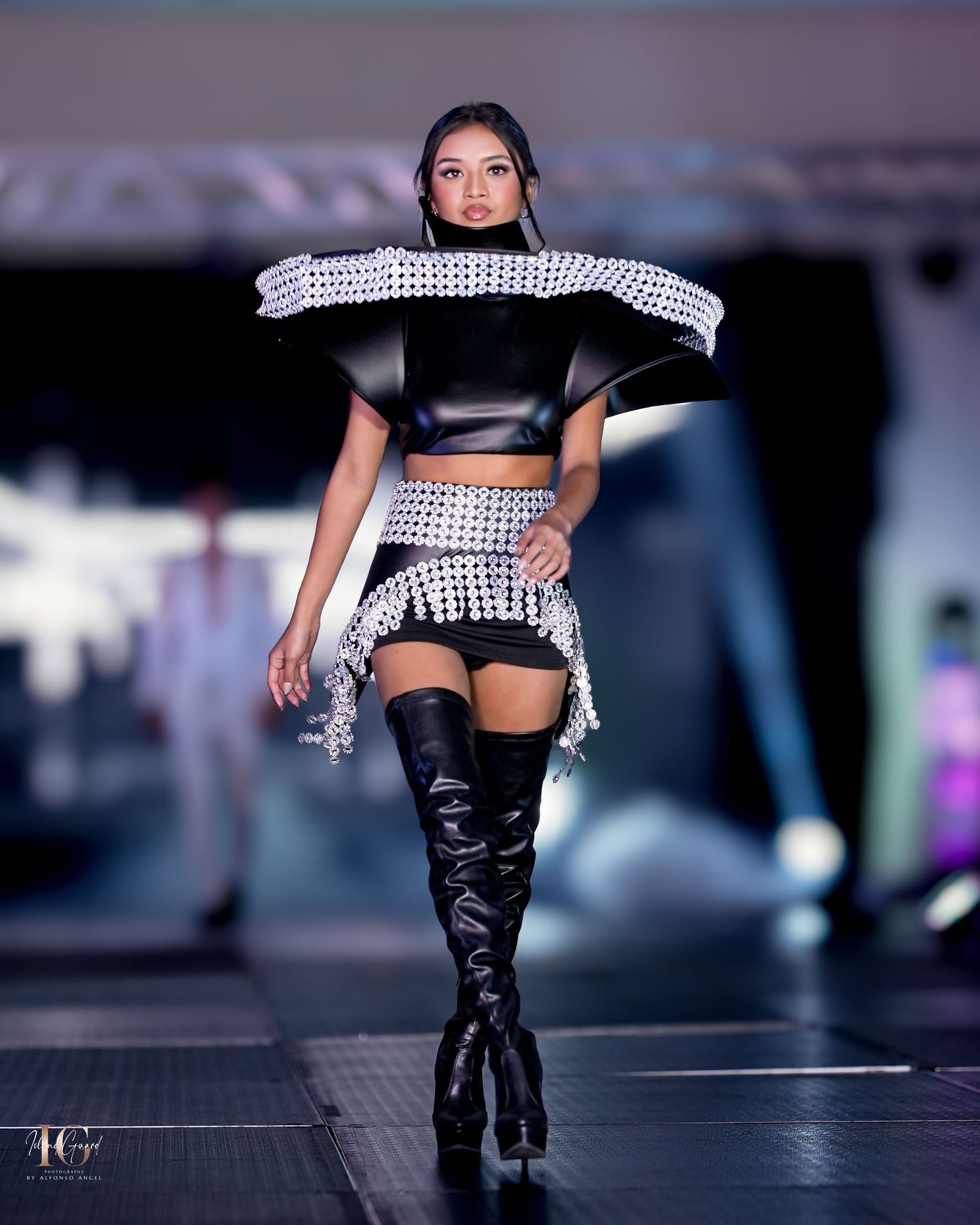 Edgy runway look featuring silver studded crop top and matching skirt with thigh-high boots.
