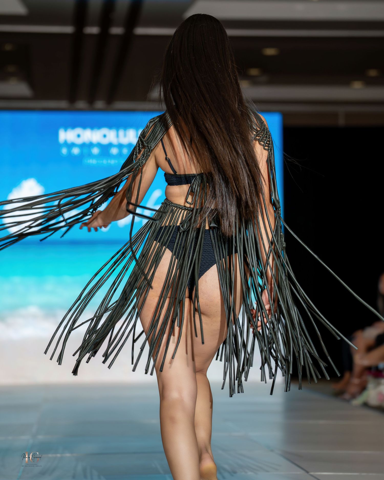 Close-up of dramatic black fringe detail on swimwear during tropical-themed fashion show.