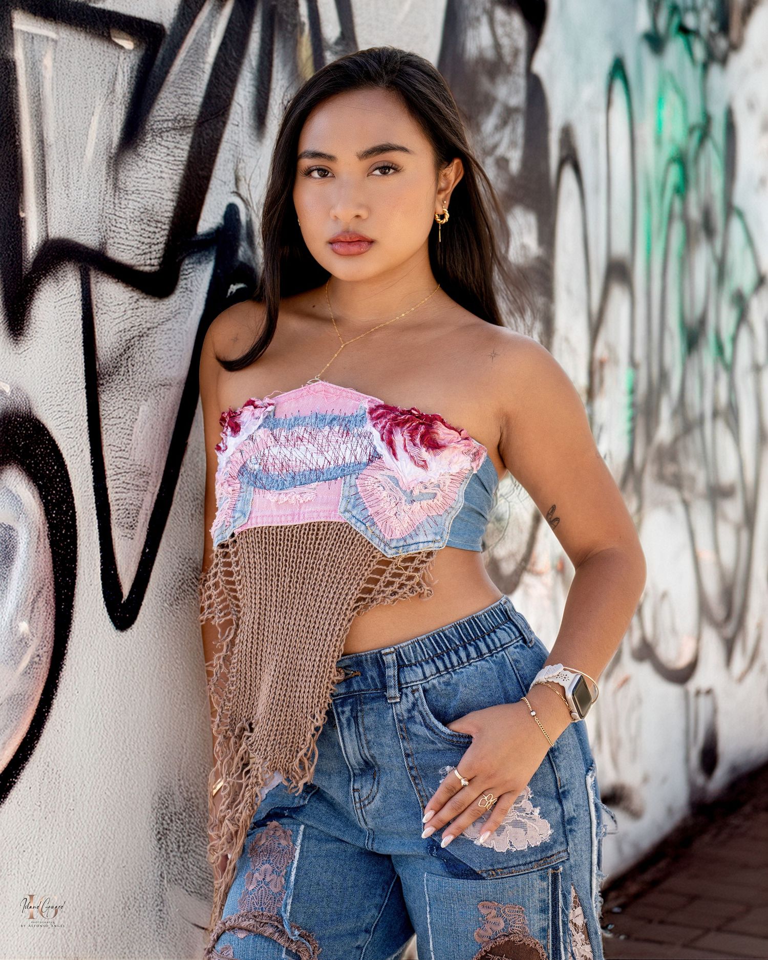 A fashionable urban portrait against a graffiti wall featuring a strapless top and distressed denim jeans.