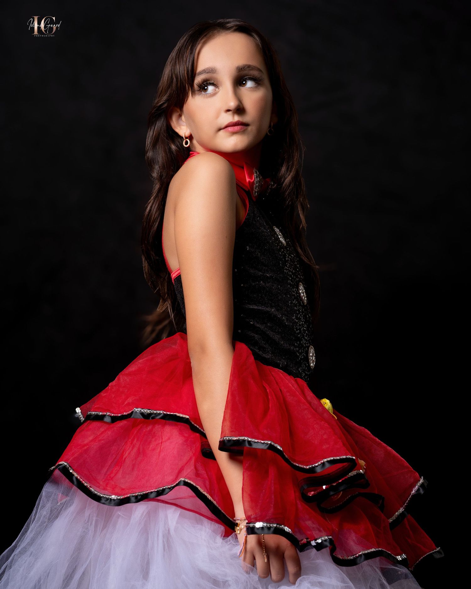 Dramatic portrait shot shows elegant figure in black and red ruffled formal gown against dark background.