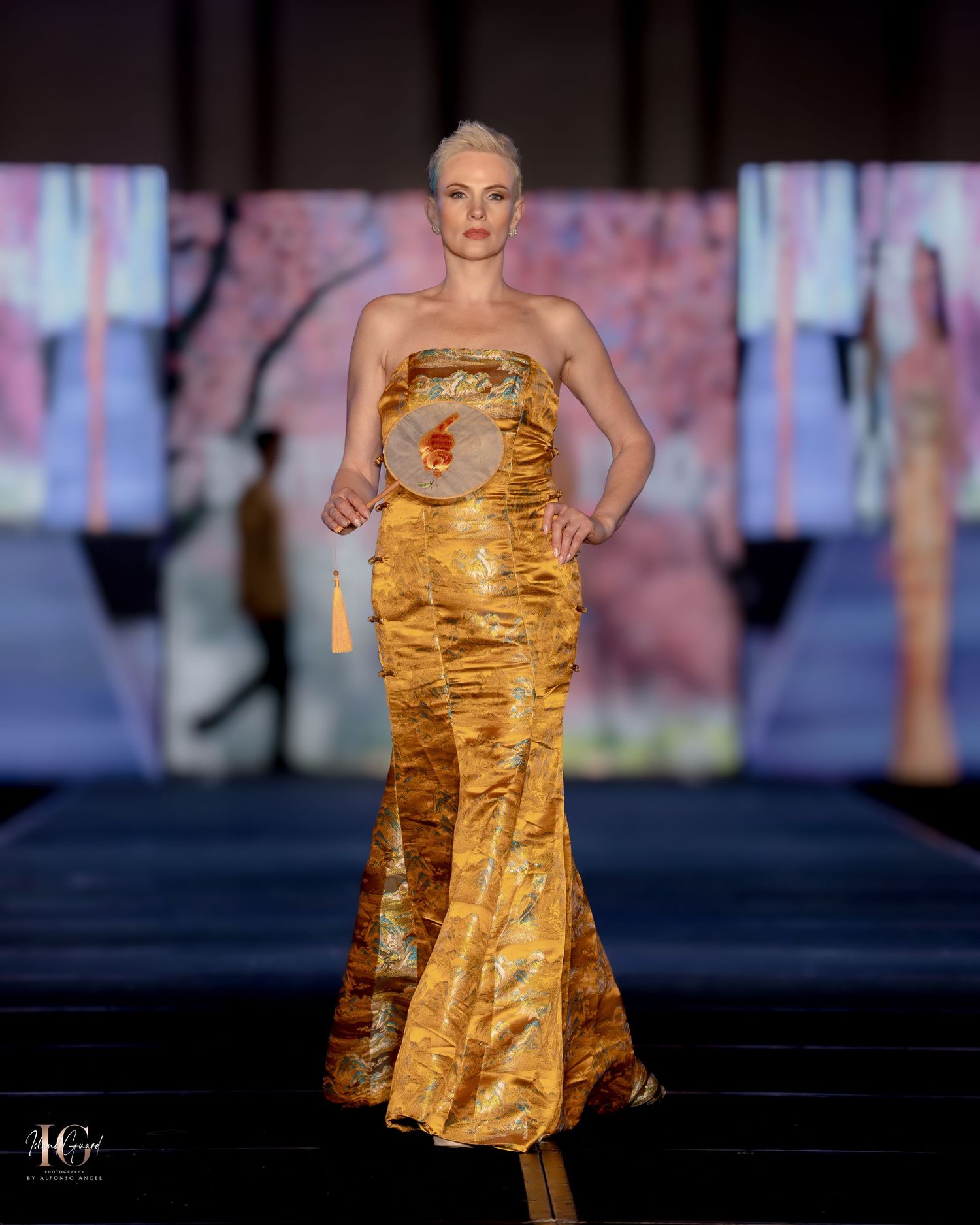 Gold metallic mermaid gown with ruched detail shown on fashion runway.