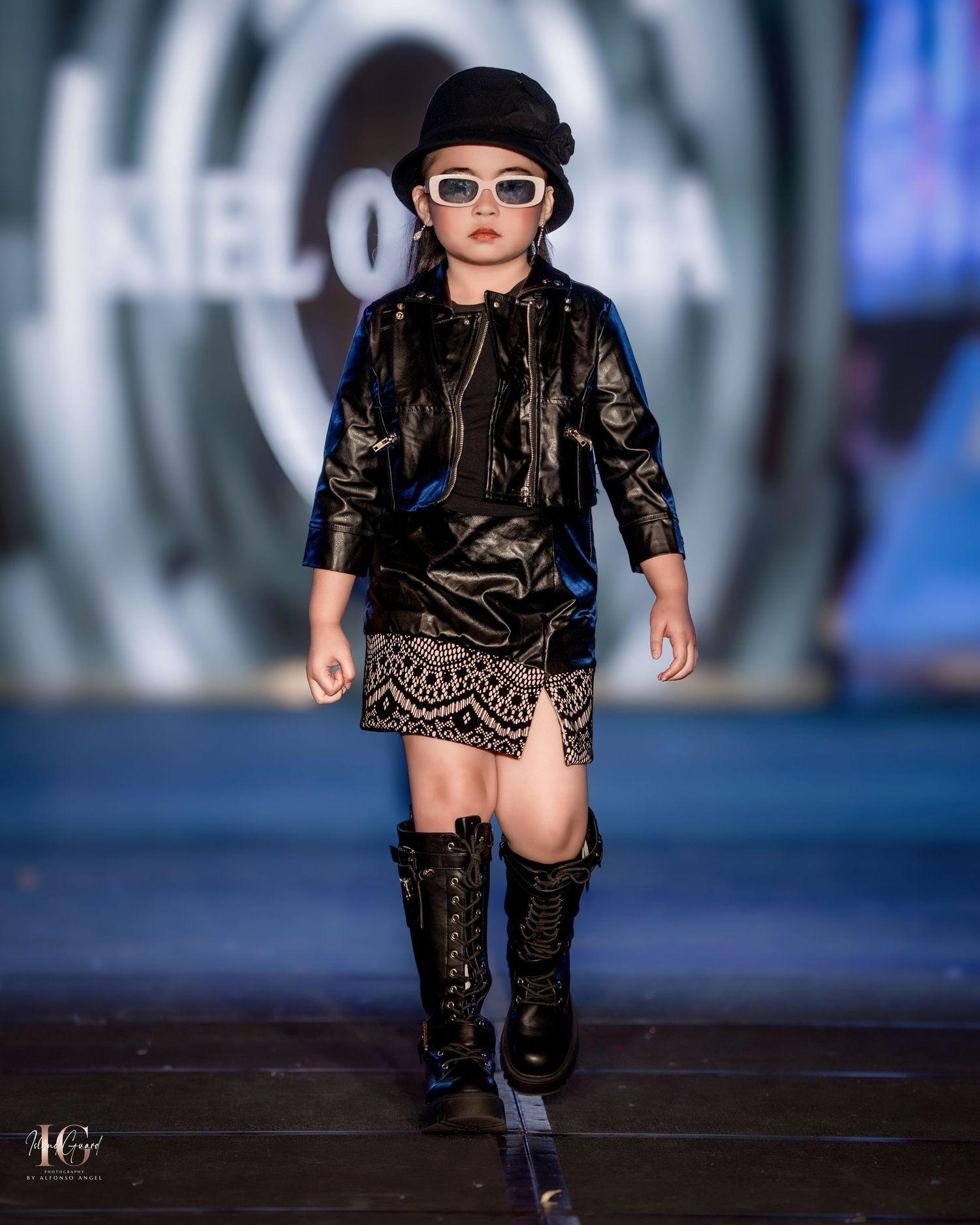 Model showcasing edgy black leather outfit with boots on modern runway stage.