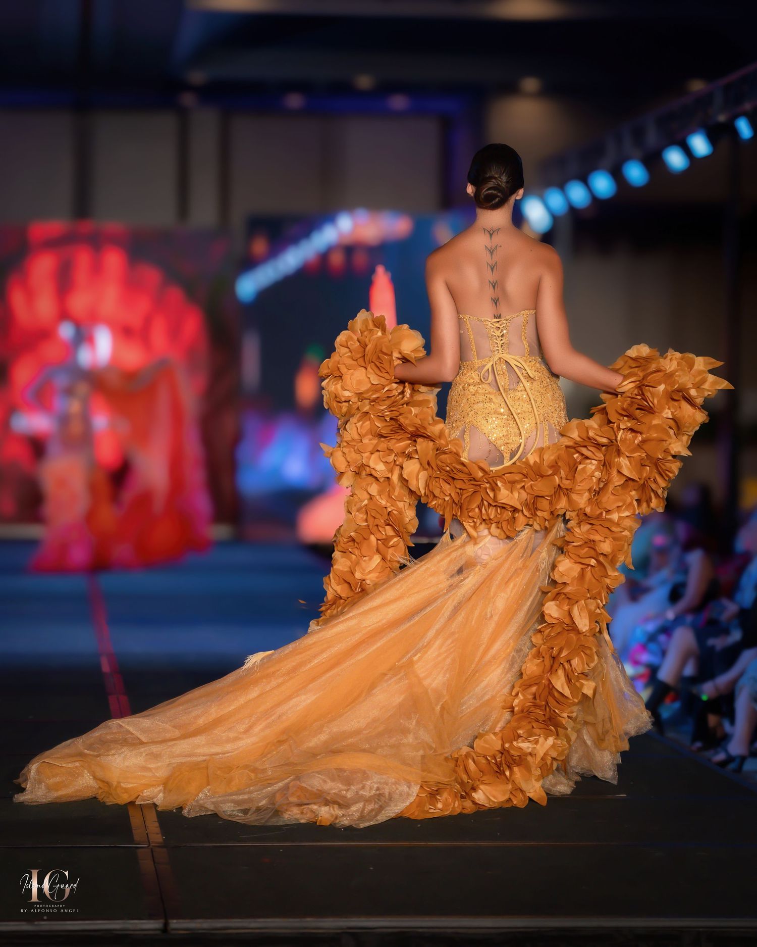 Dramatic orange ruffled ball gown with flowing train showcased on dark runway.