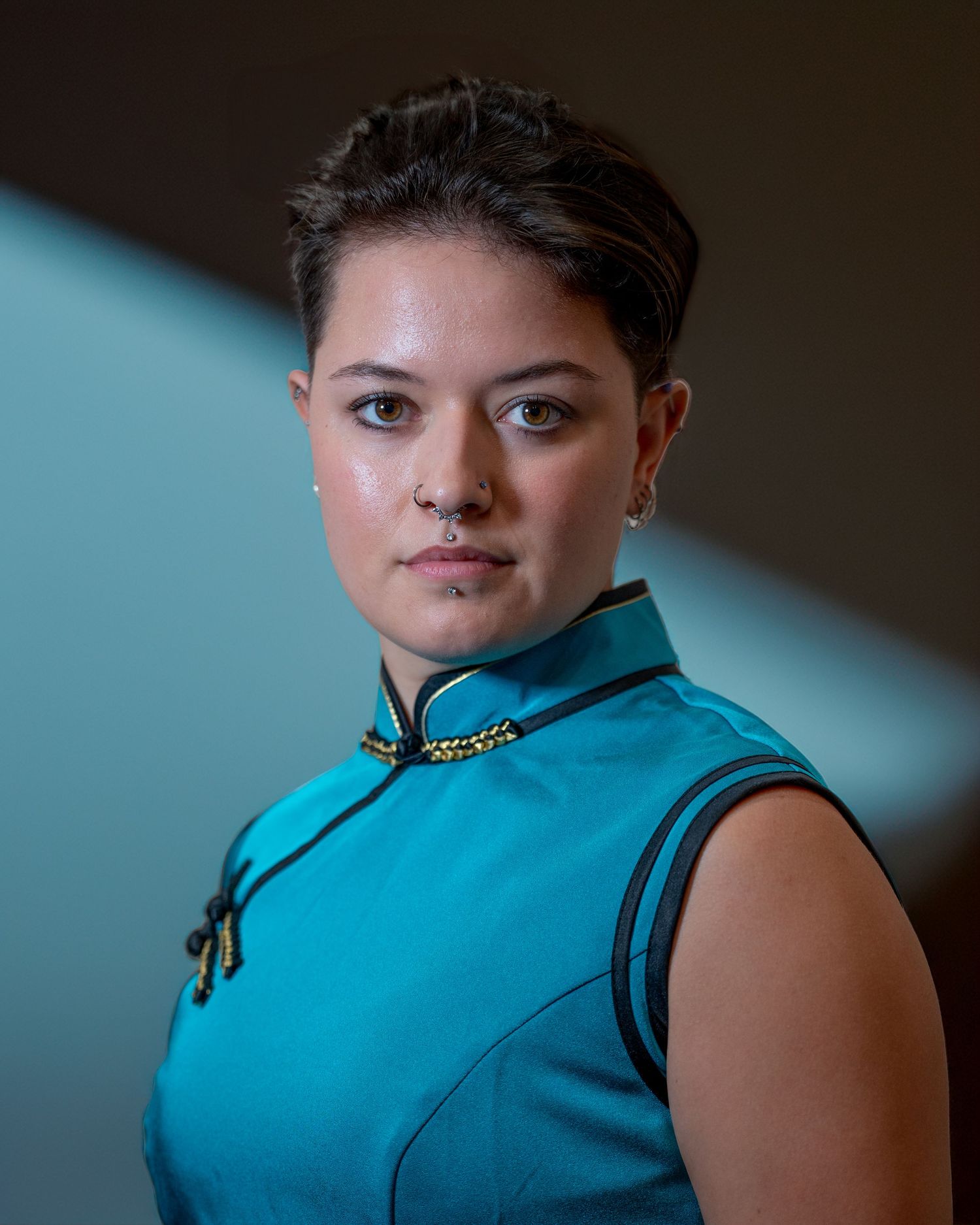 Model wearing a teal qipao-style top poses in dramatic lighting against dark background to showcase Asian fashion.