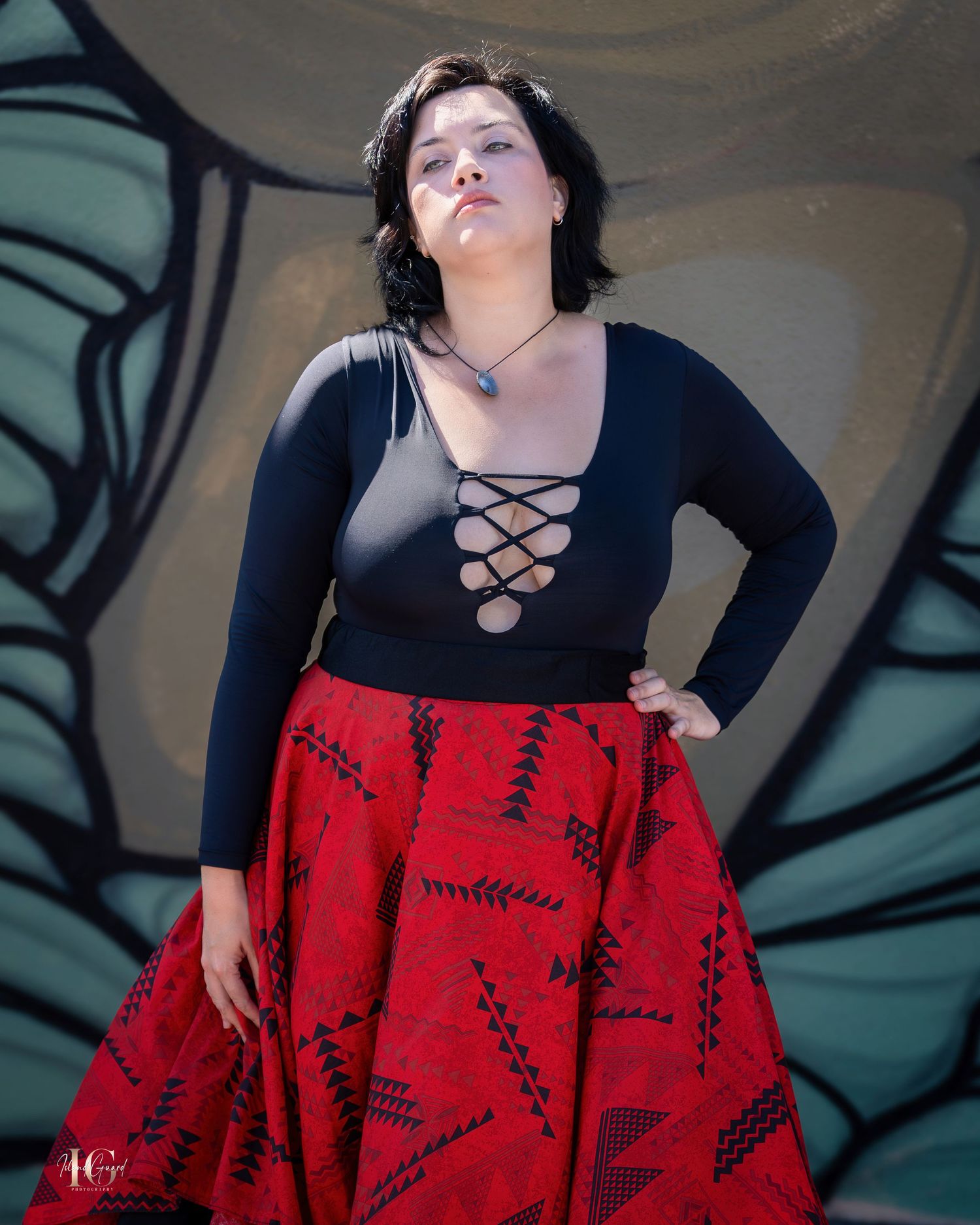 Model wearing black top and red patterned skirt poses dramatically against mural backdrop.