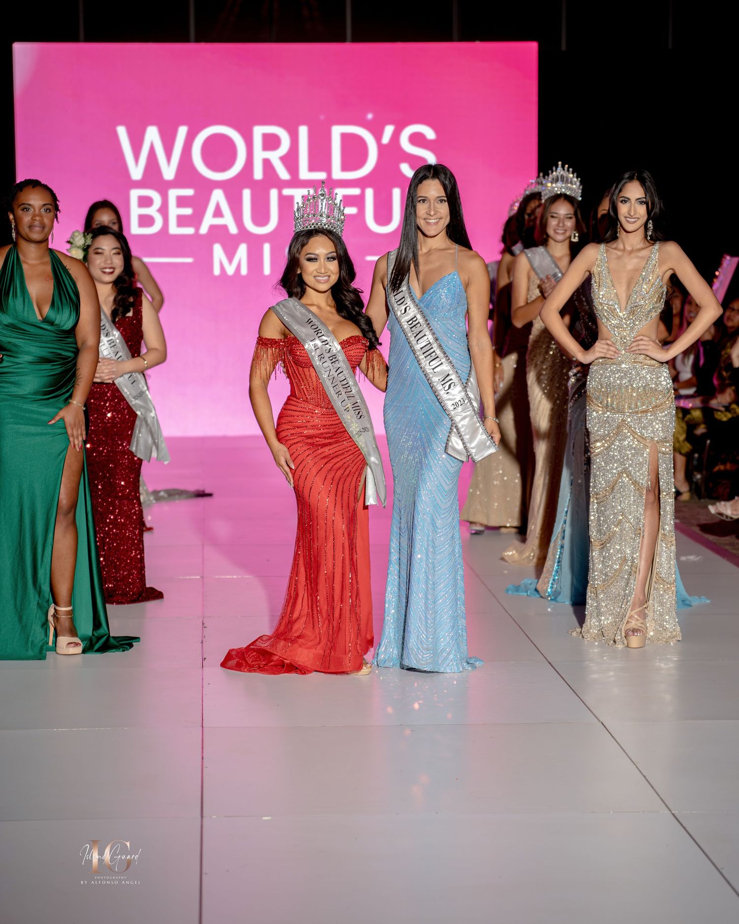 Beauty pageant contestants in elegant evening gowns pose on a pink-lit runway stage during a competition event.