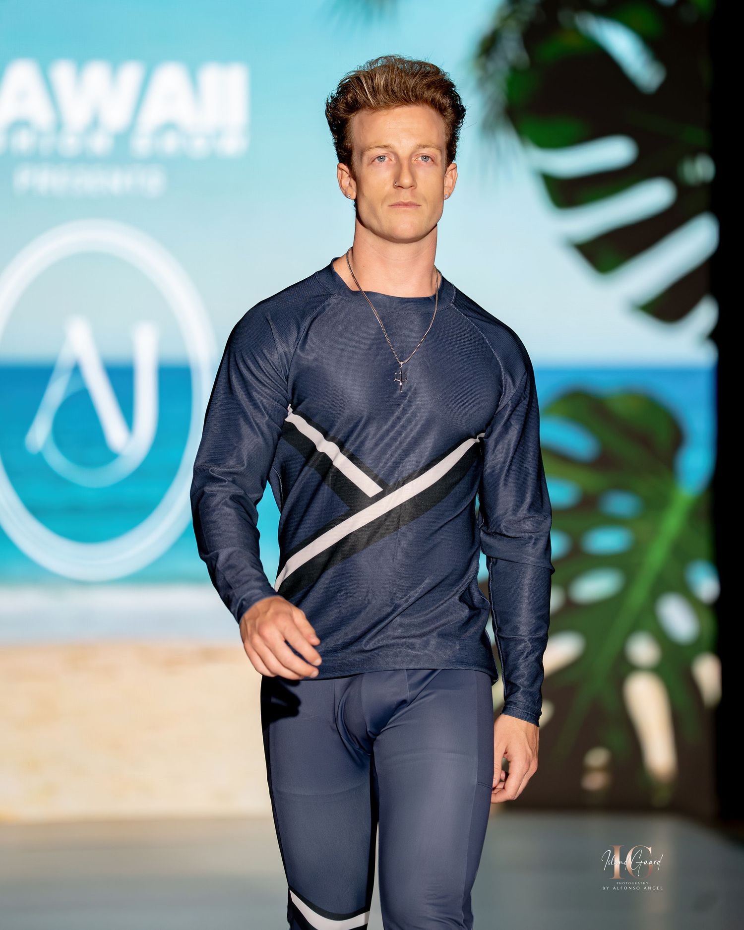 Model walks runway in navy blue athletic wear with white diagonal stripe detail at fashion show.
