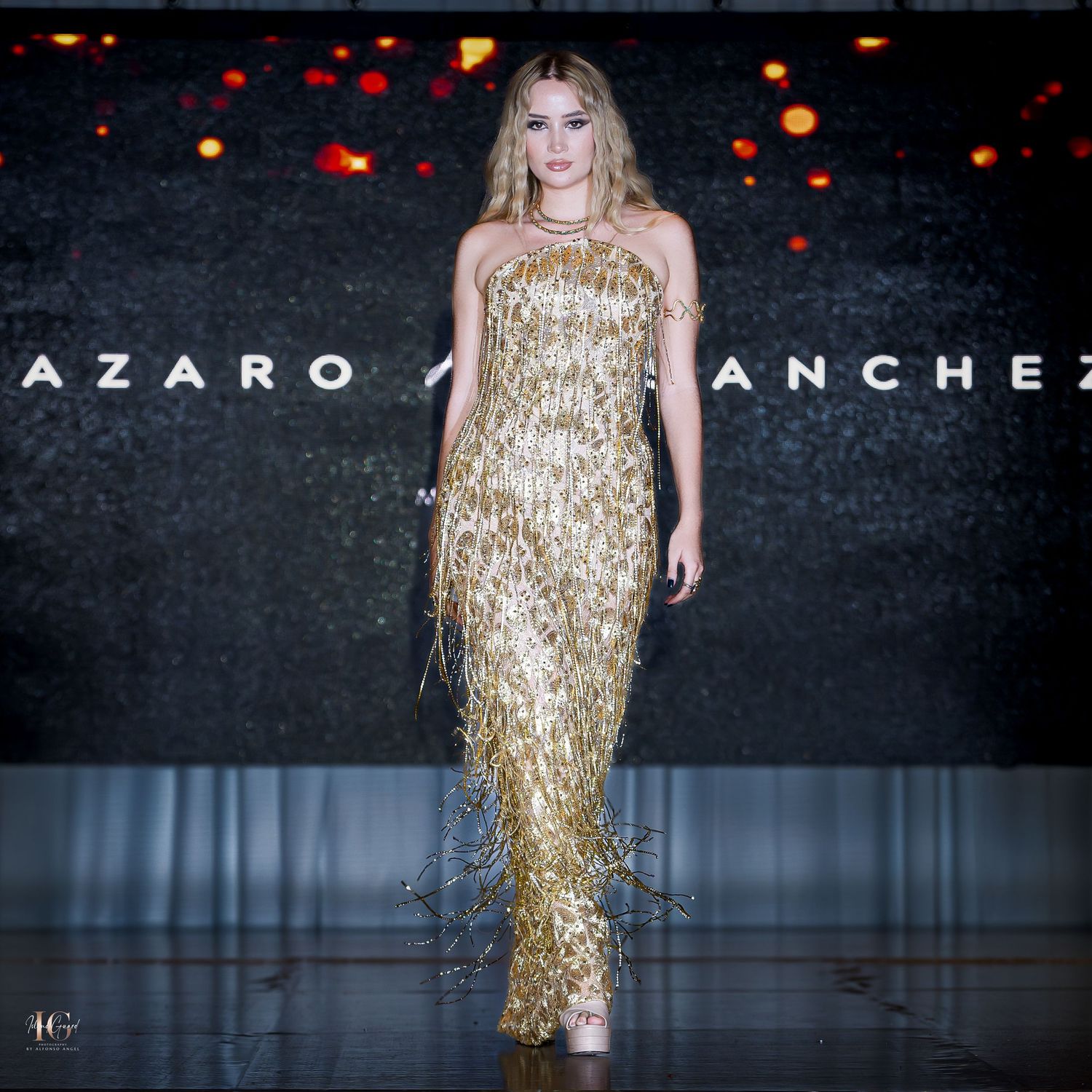 Model wearing gold sequined gown walks runway at Lazaro Sanchez show.