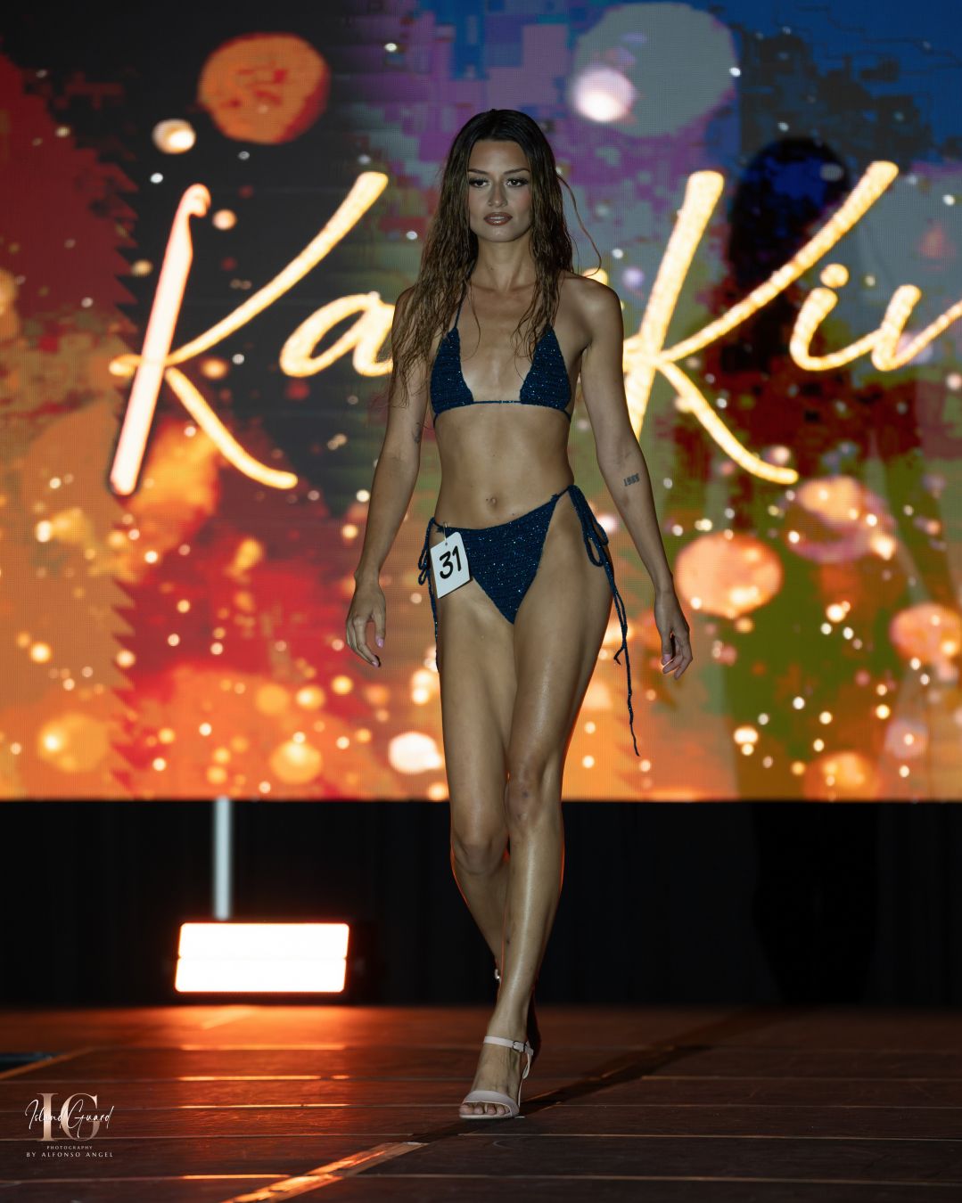 Model in navy blue swimsuit performs catwalk walk with colorful light effects.