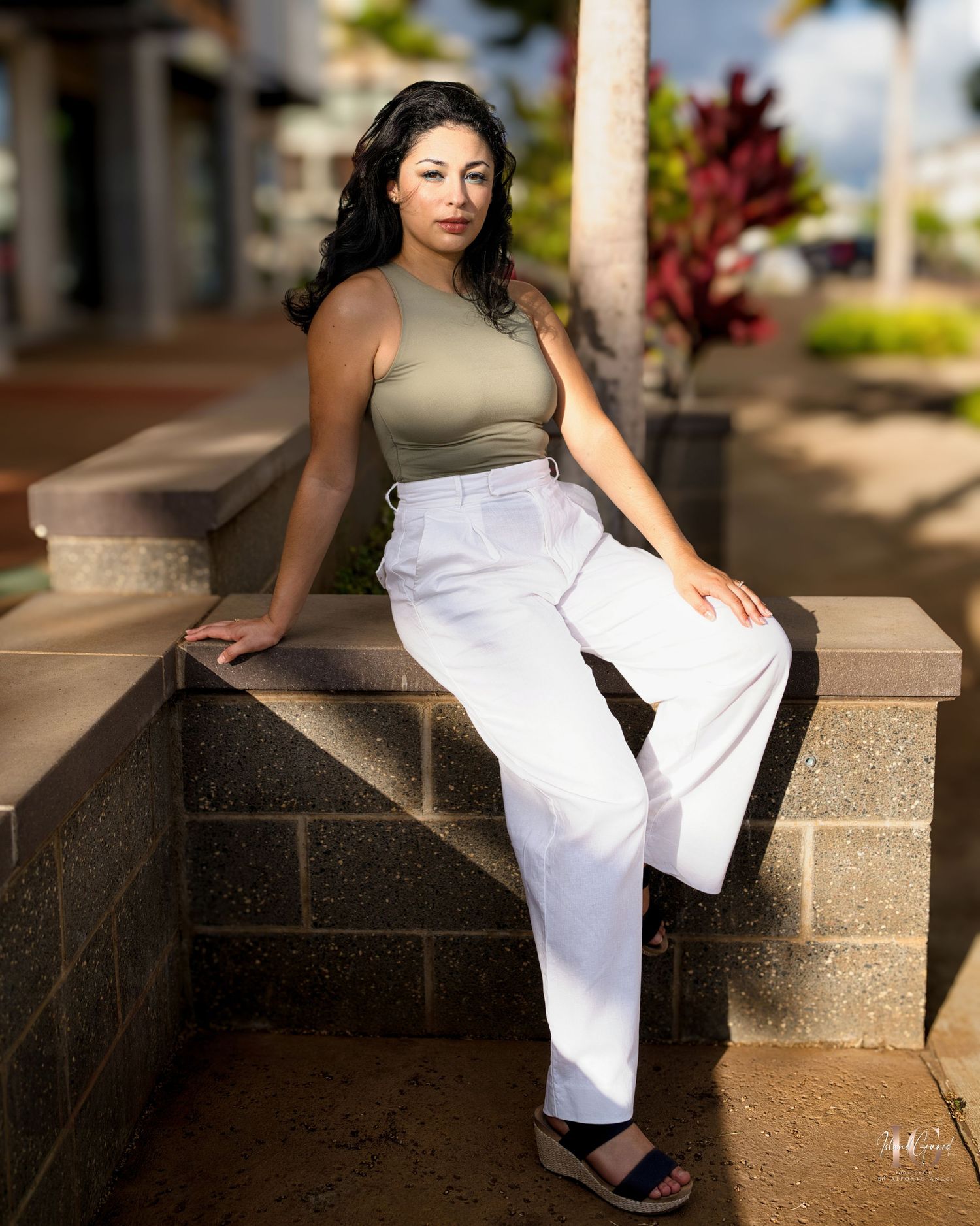 Person in white flowing dress and tan top sitting gracefully on outdoor stone steps in garden setting.
