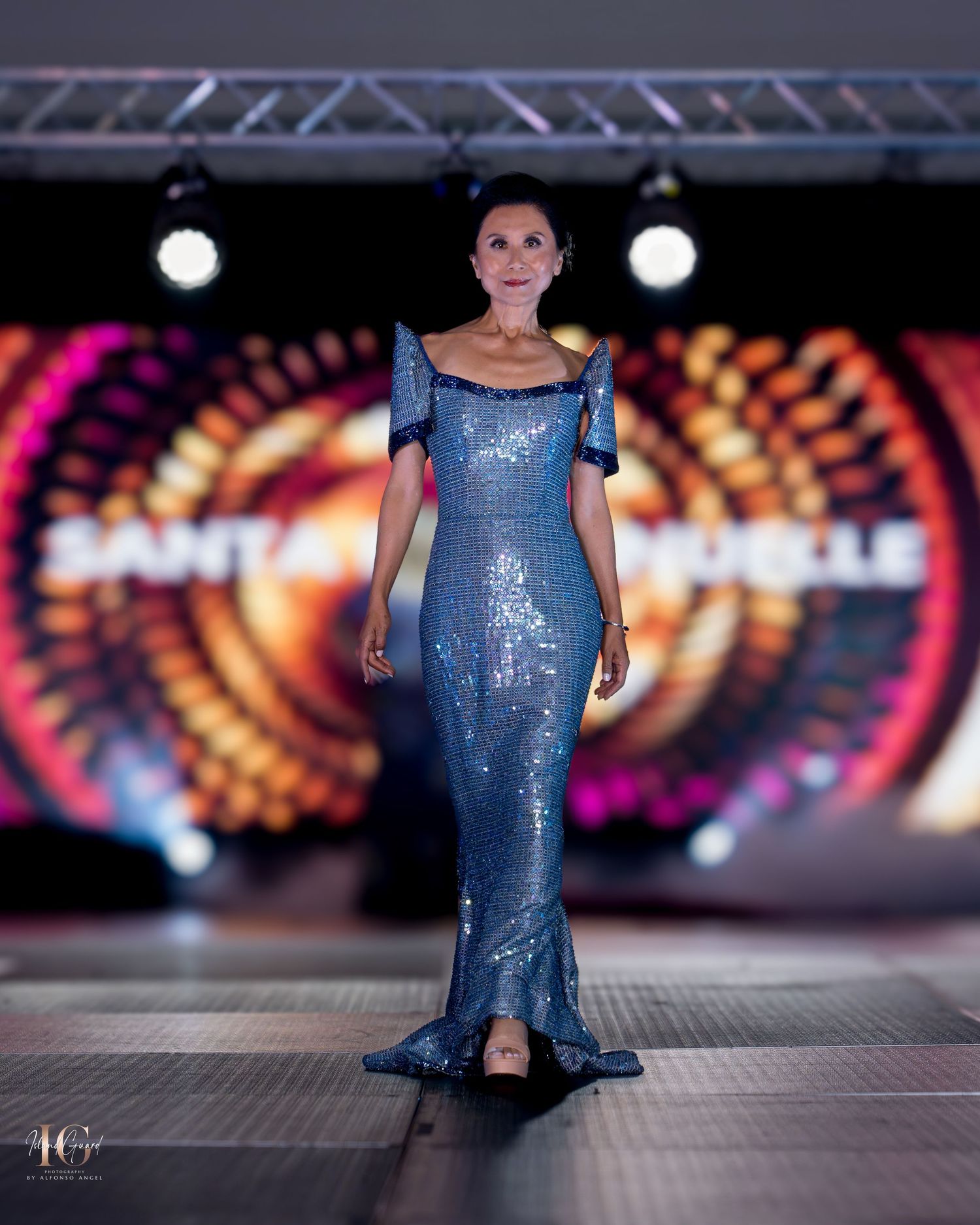 Shimmering blue fitted evening gown with mermaid silhouette presented on illuminated runway.