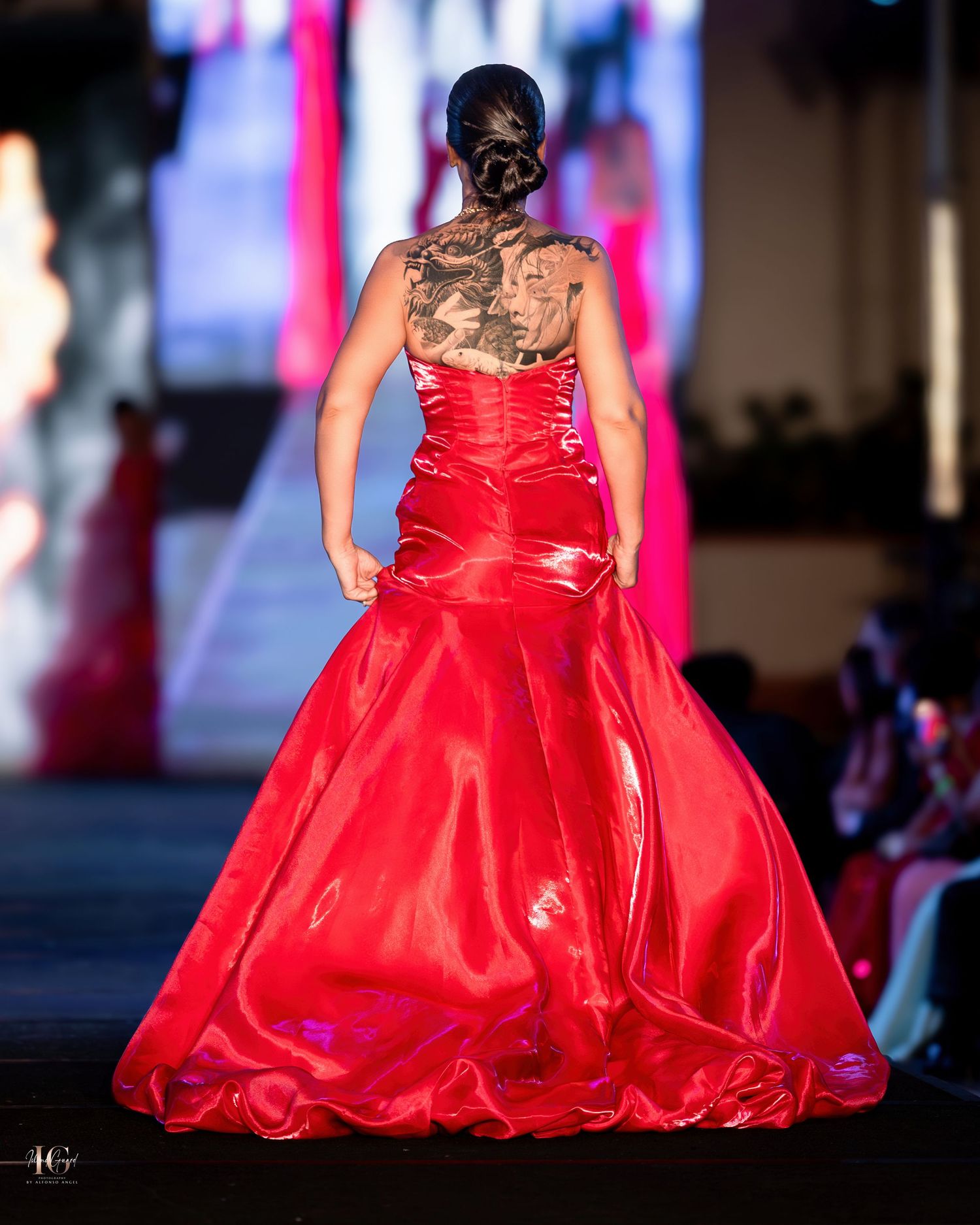 Back view of red satin evening gown with gathered details and full skirt on fashion catwalk.
