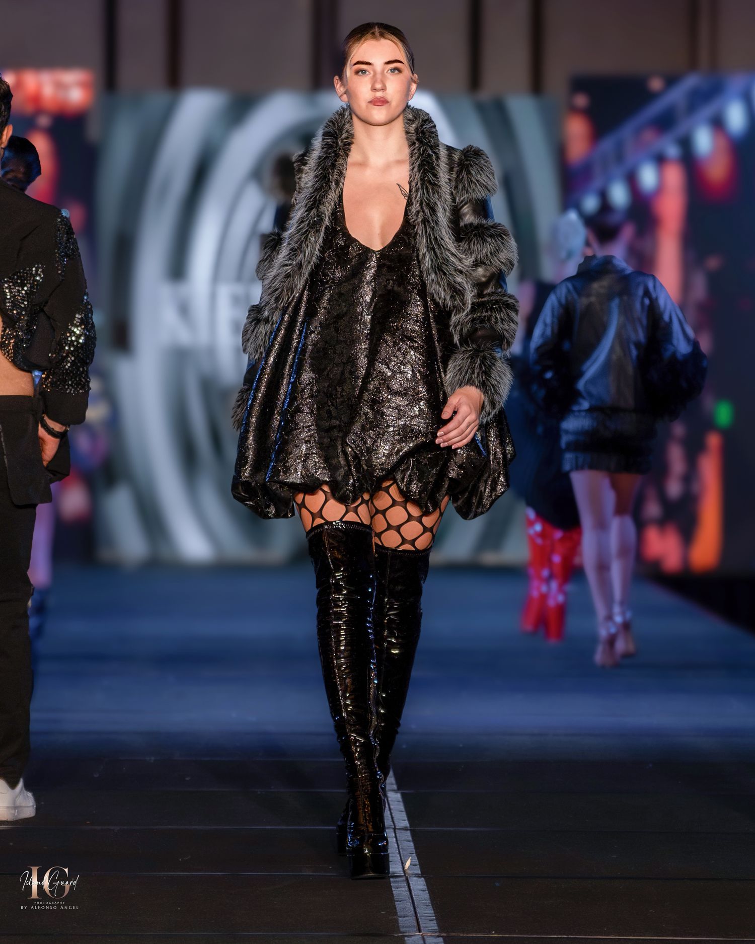 Model in black fur coat and thigh-high boots walking runway with futuristic circular backdrop.
