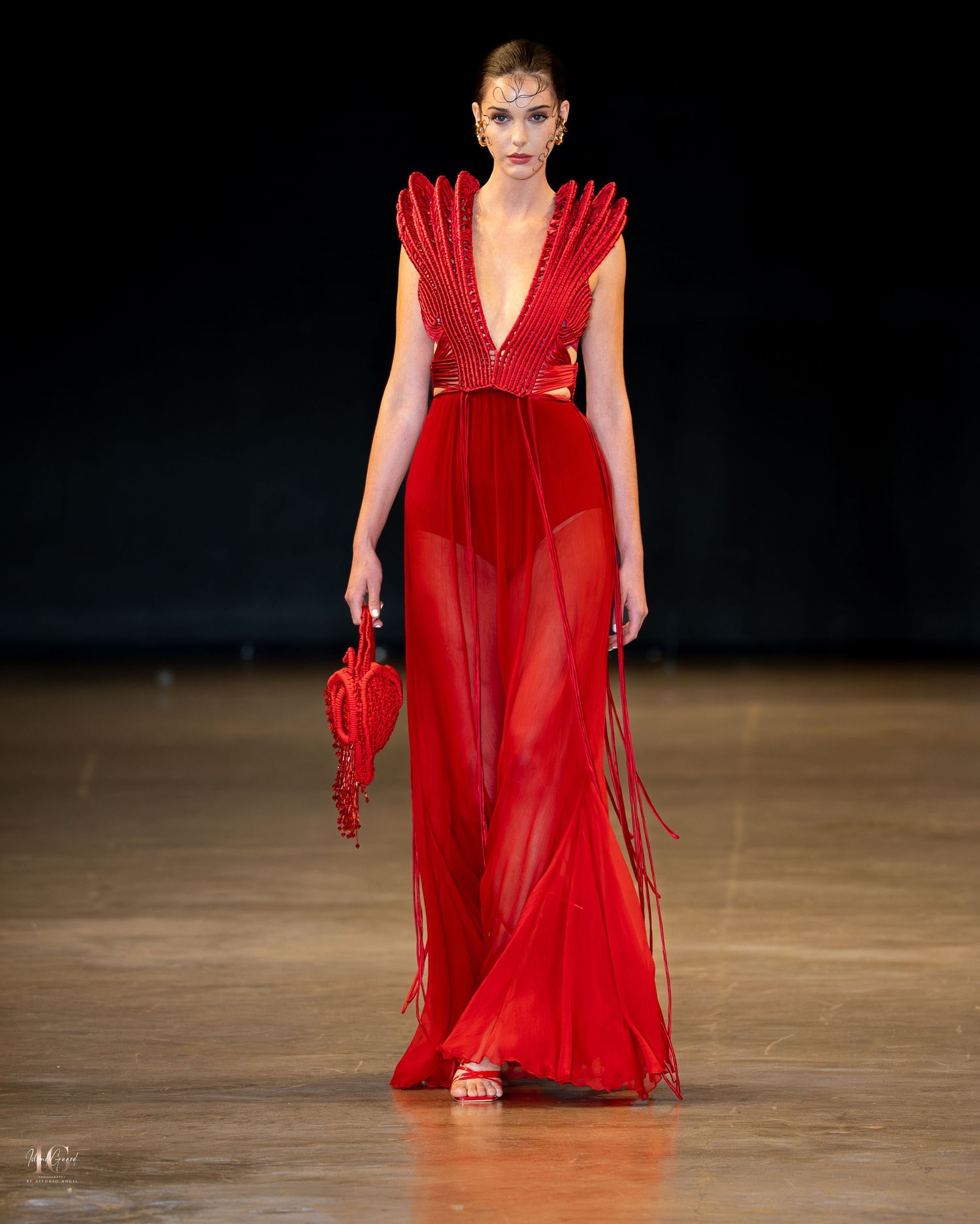 Models walk the runway in flowing red evening gowns during a fashion show presentation.