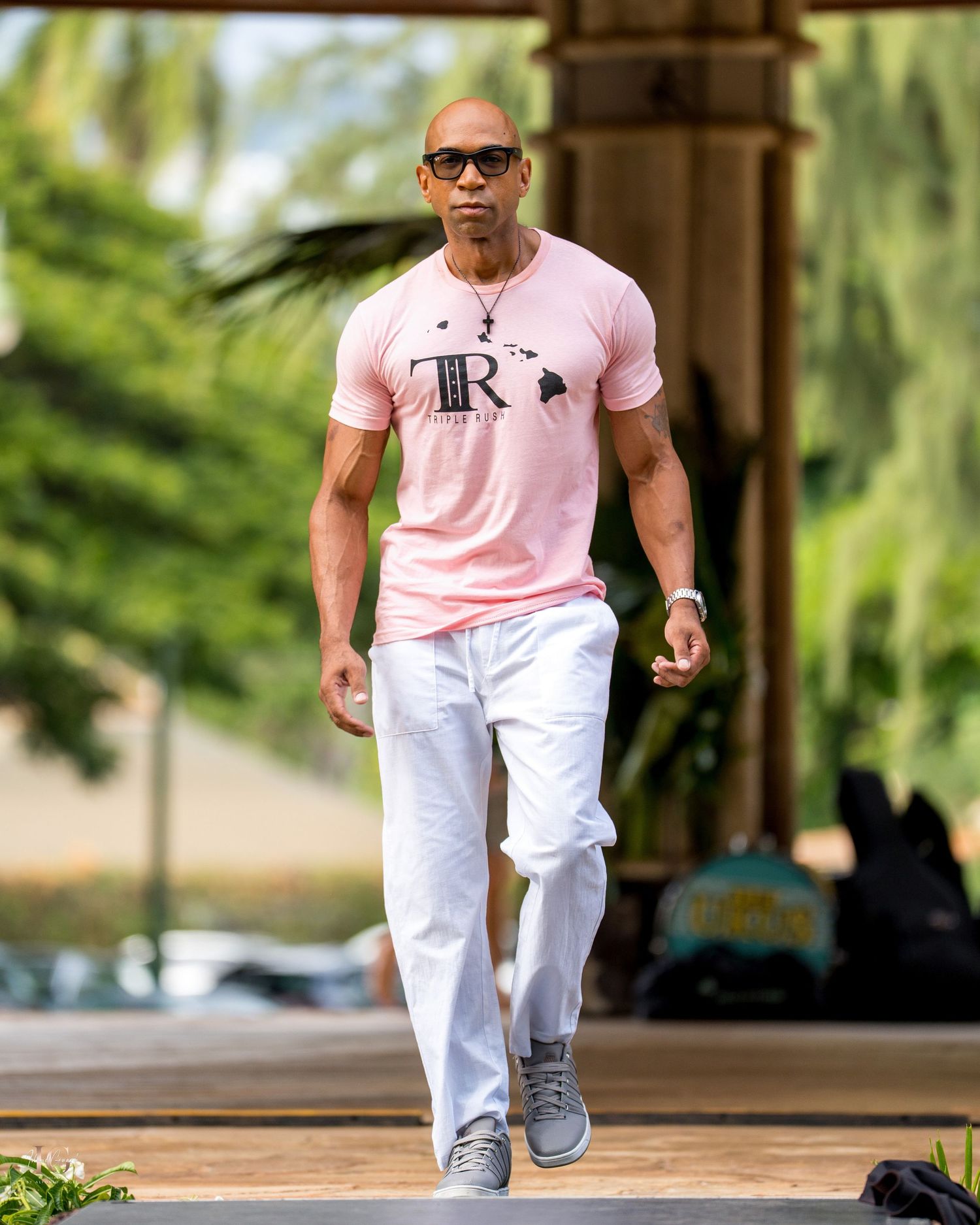 Person in pink shirt and white pants walking on a path with trees and greenery in the background.