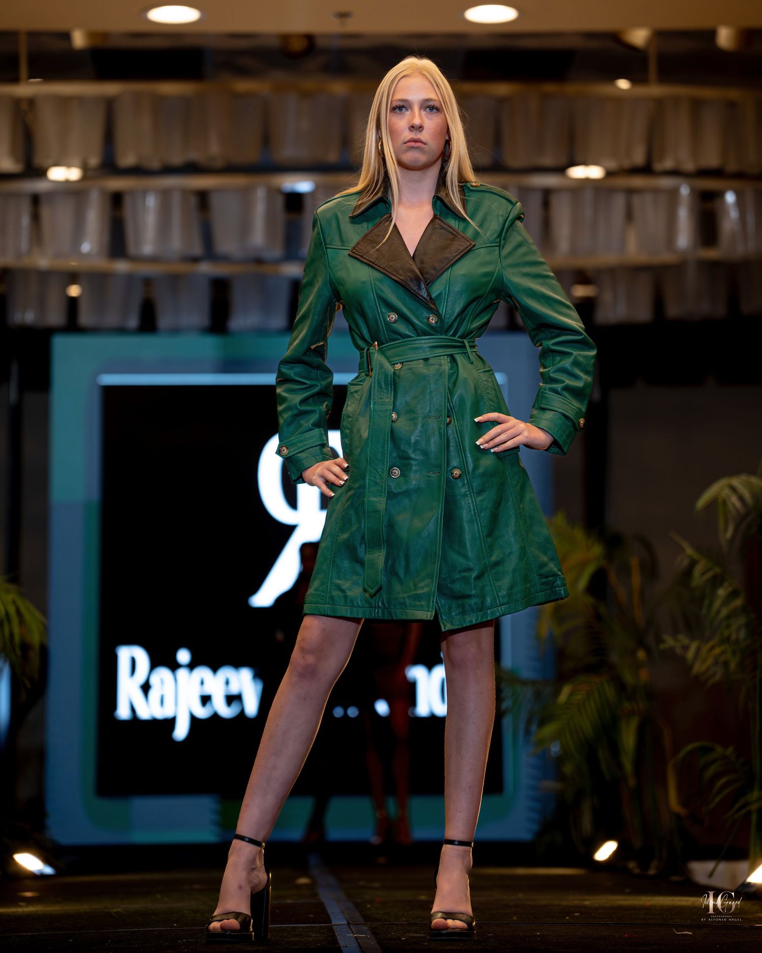 Model showcases emerald green satin blazer jacket on fashion runway under dramatic lighting.