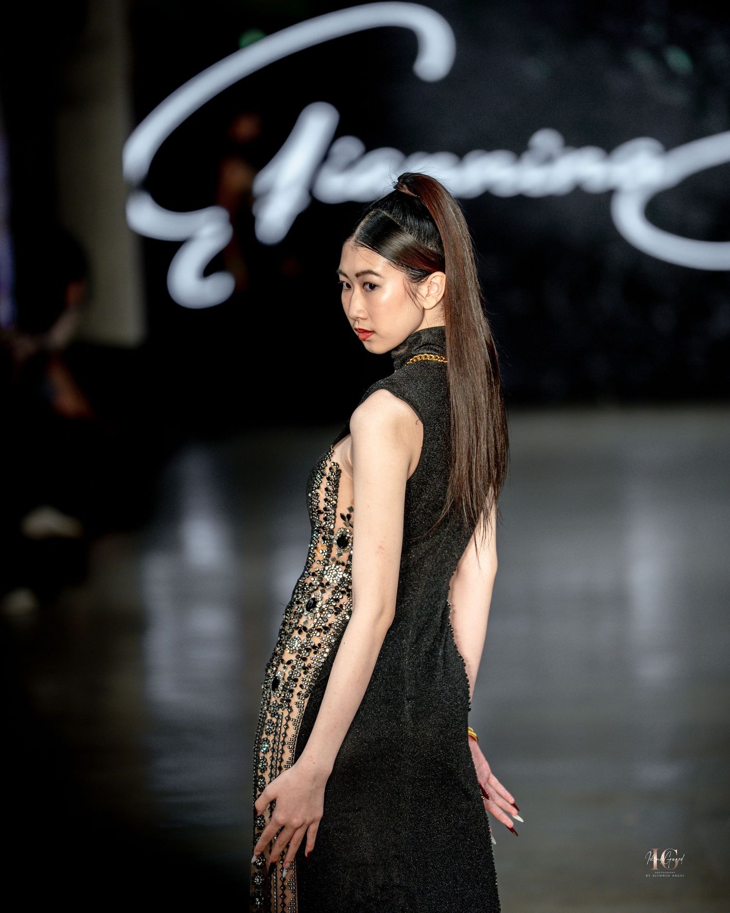 Model walks runway in black evening gown and leopard print shawl during fashion show.