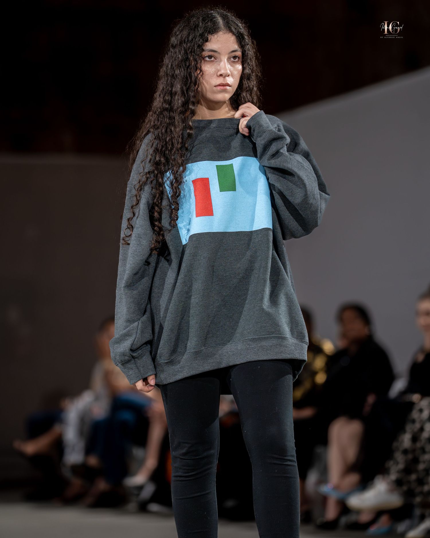 Model walks runway in oversized gray sweatshirt and dark pants during fashion show.