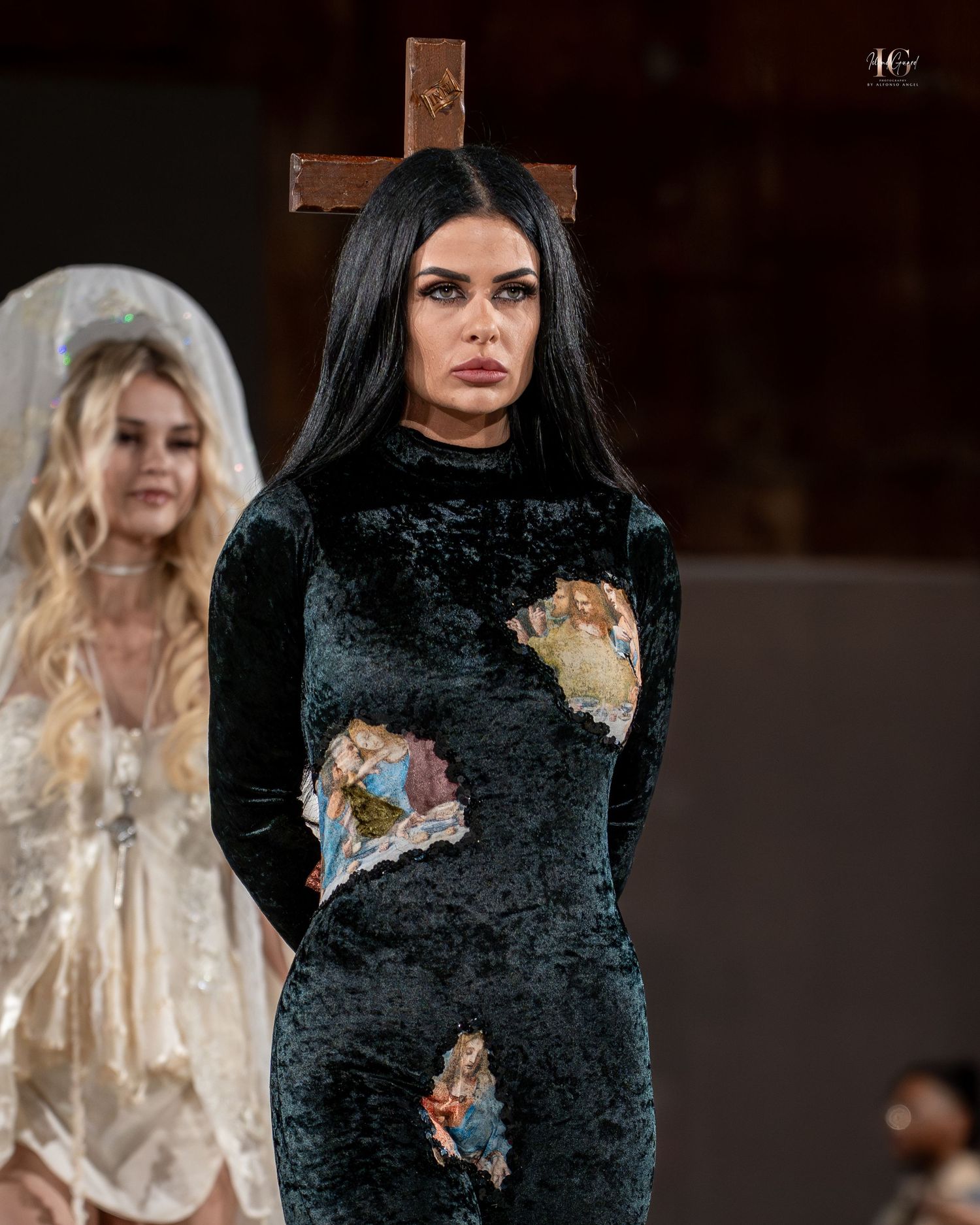 Gothic fashion runway show featuring a black velvet dress with religious cross imagery and distressed details.
