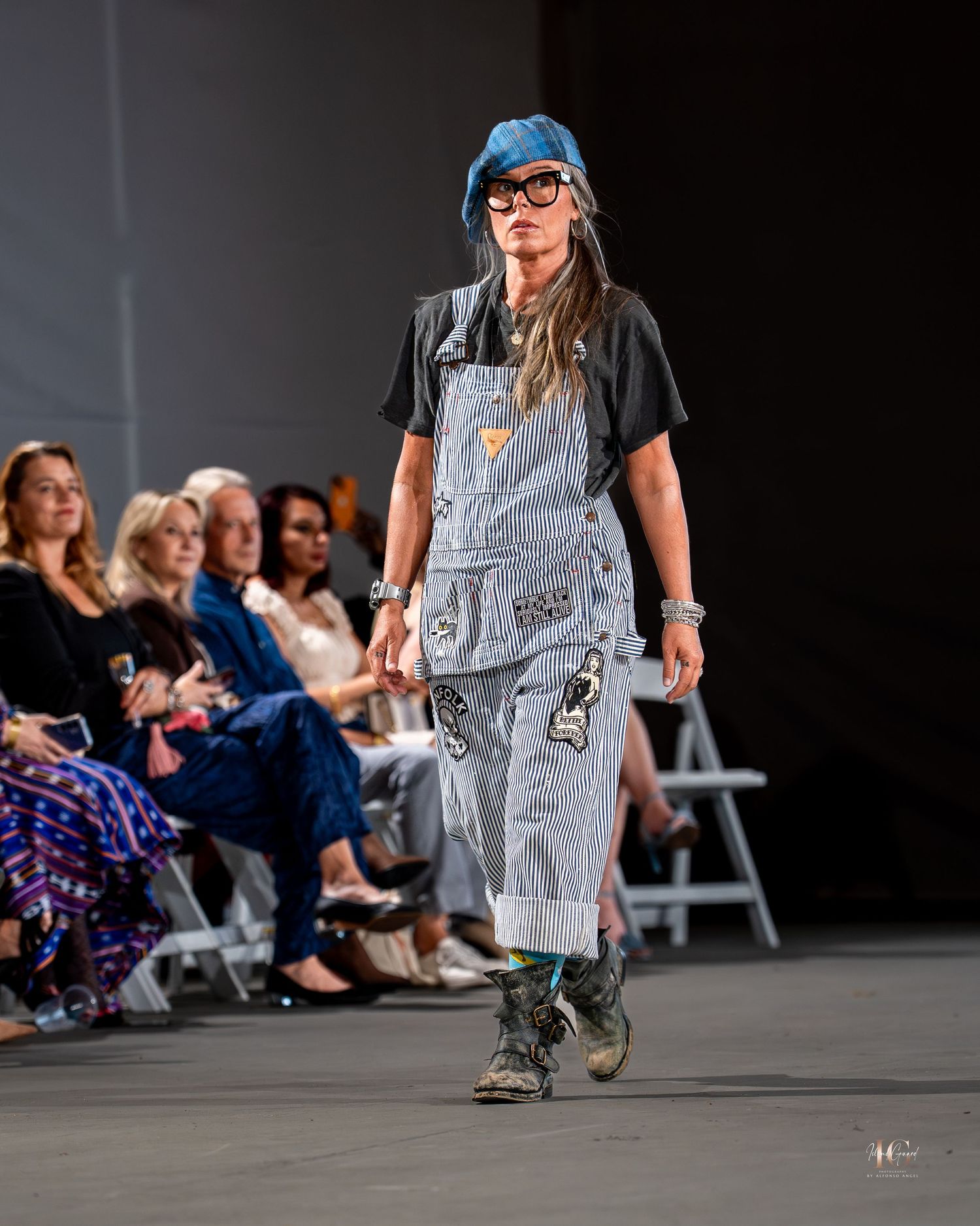 Models showcase contemporary fashion designs on a sleek runway with audience members seated along the sides.