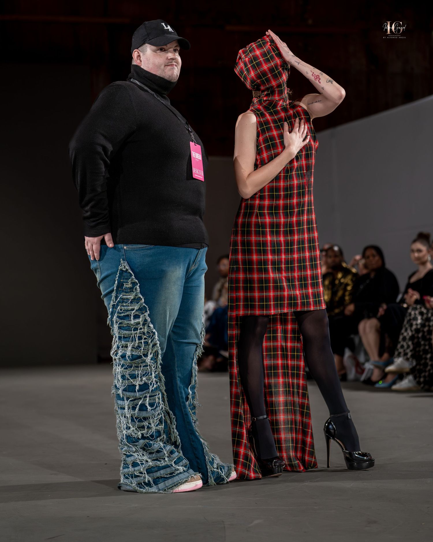 Two performers in contrasting outfits of plaid and solid black move together on a dark stage during a dance performance.
