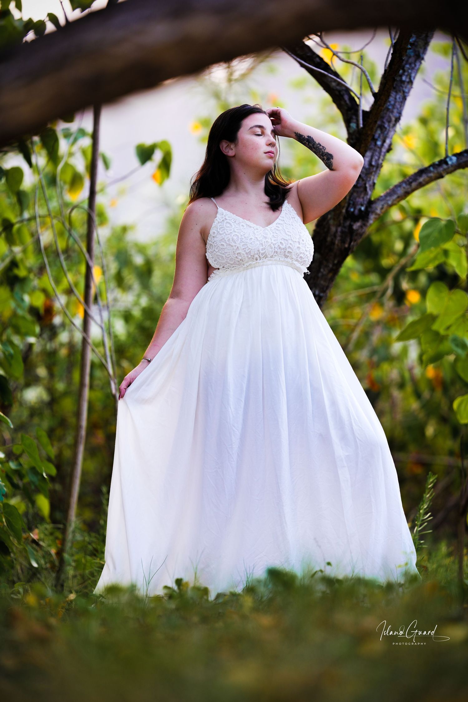 A flowing white empire waist gown is photographed in a natural outdoor garden setting with green foliage.