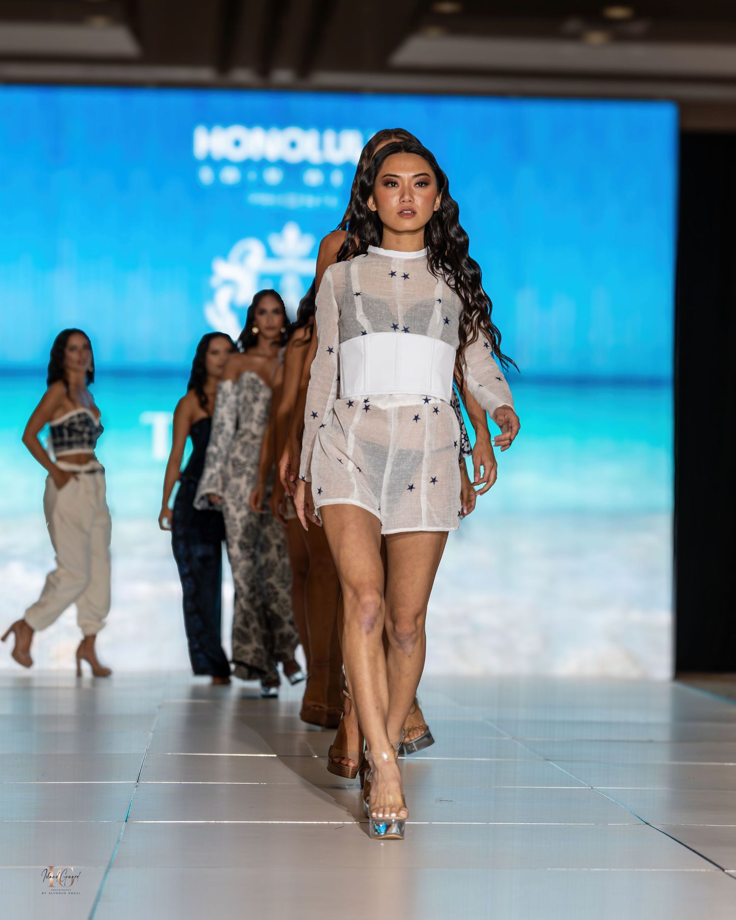 Sheer white overlay dress with minimalist design presented at beach-themed fashion show.